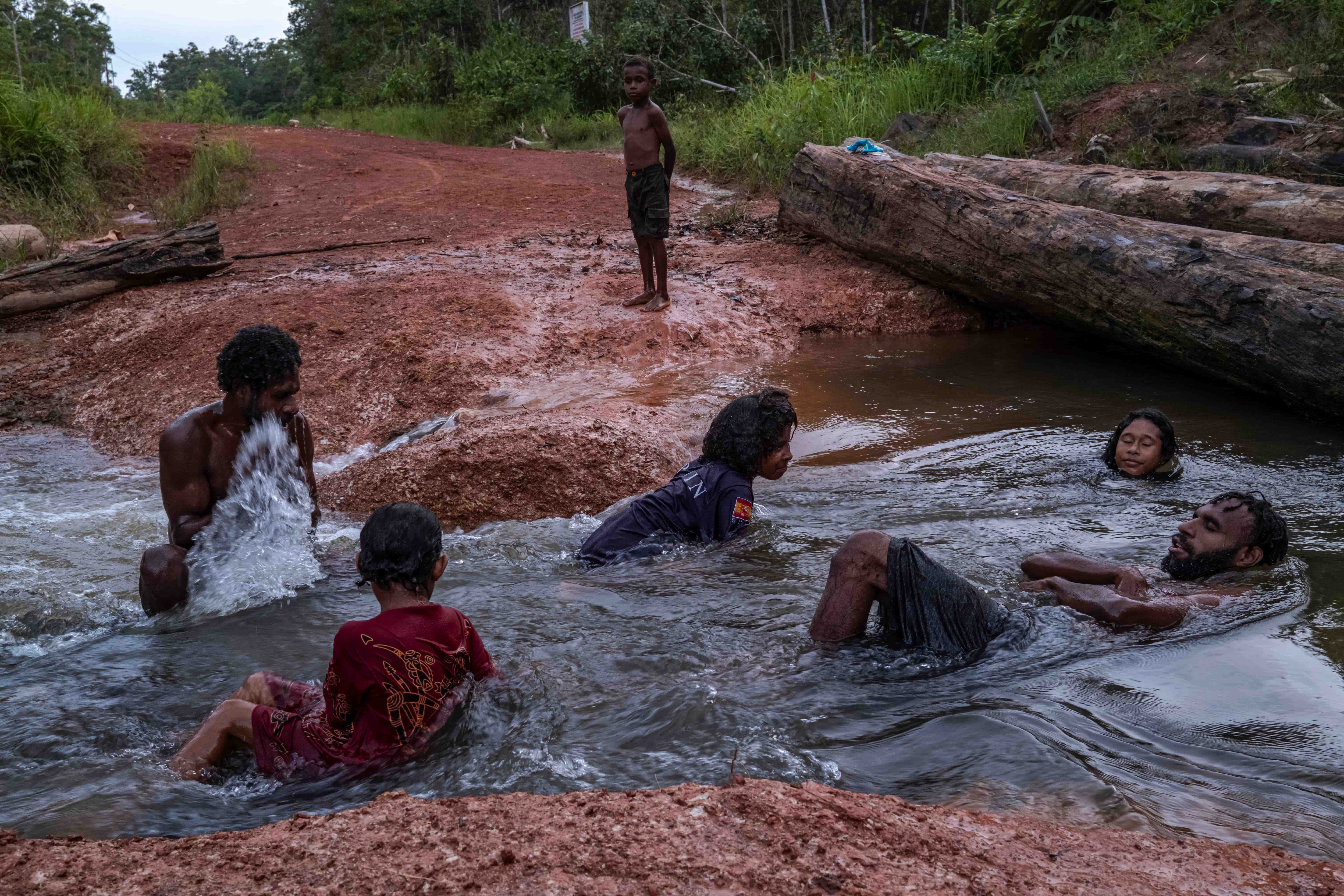 Men and children sit in a river.