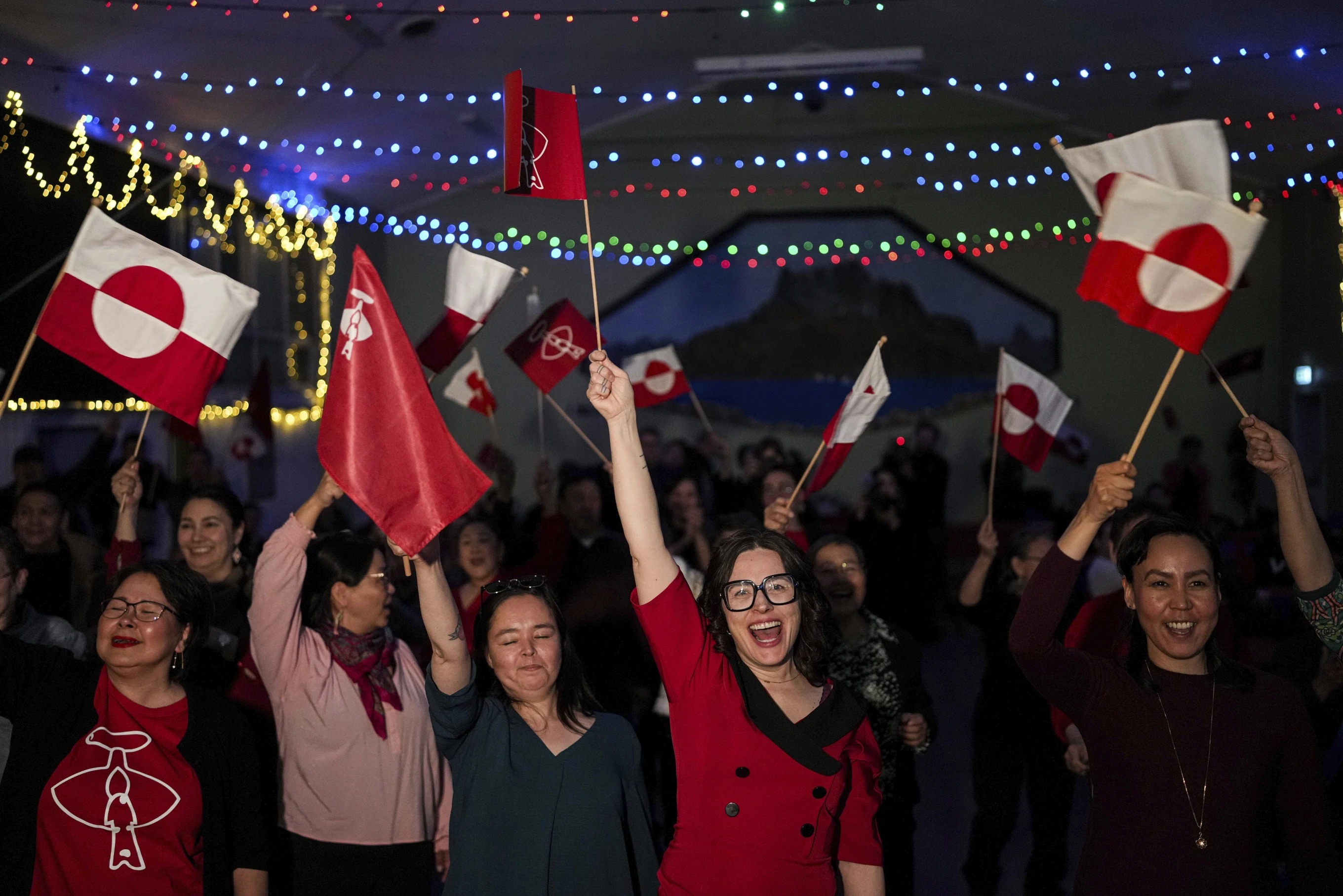 Smiling women in a room lined with lights wave red-and-white flags. 