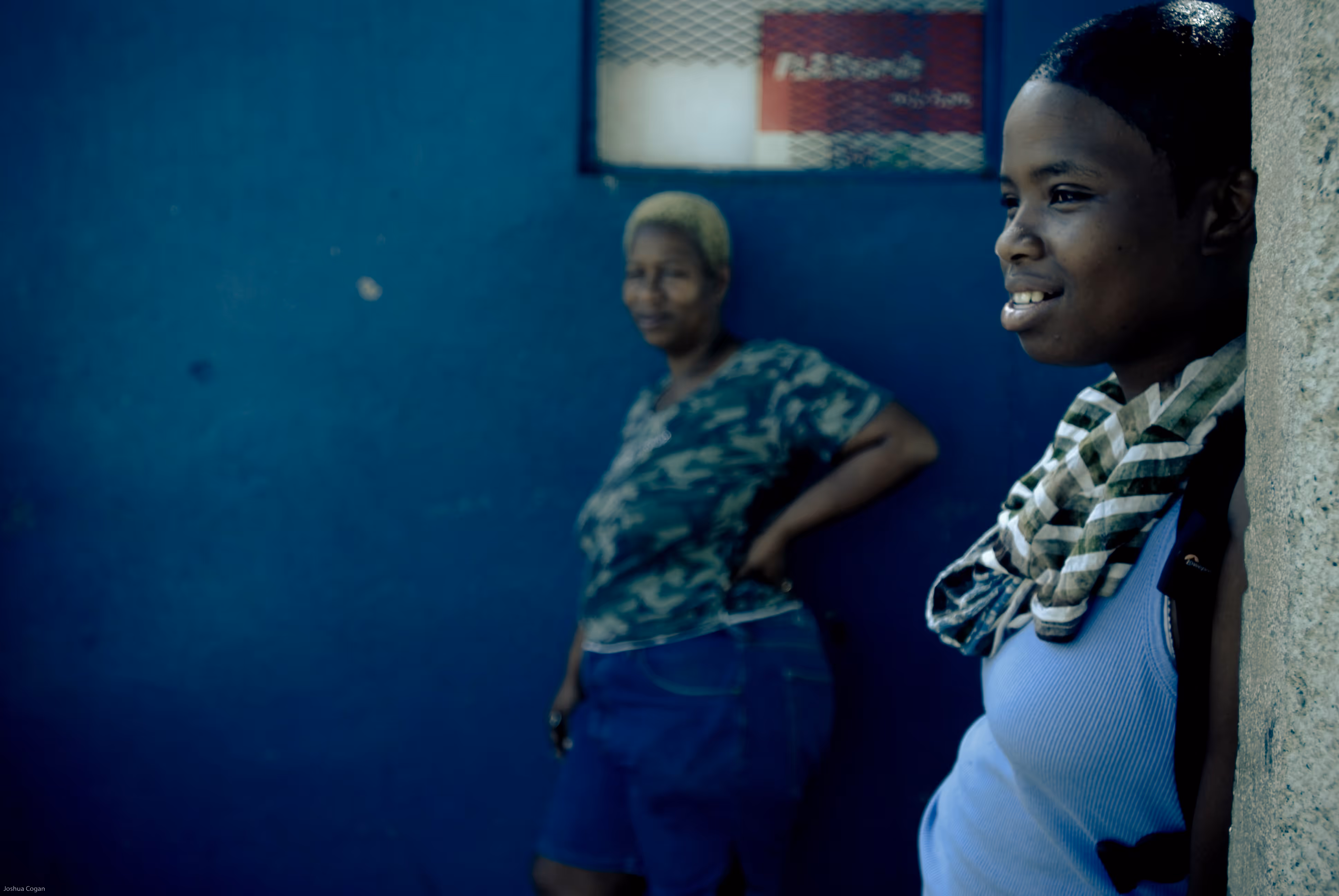 An older woman in the background looks lovingly at a younger woman in the foreground