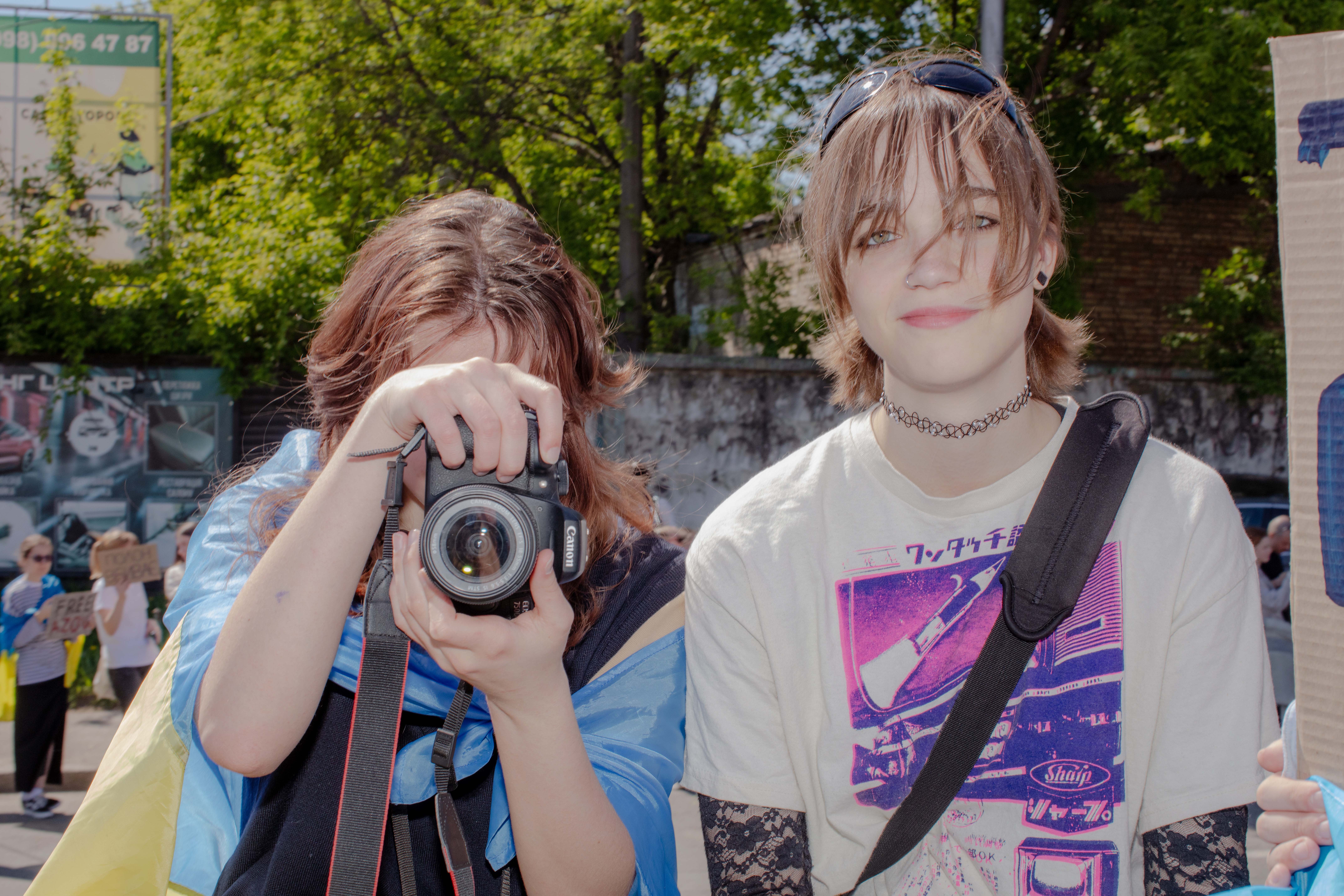 Two young people face the camera. One of them also has a camera trained at the viewer