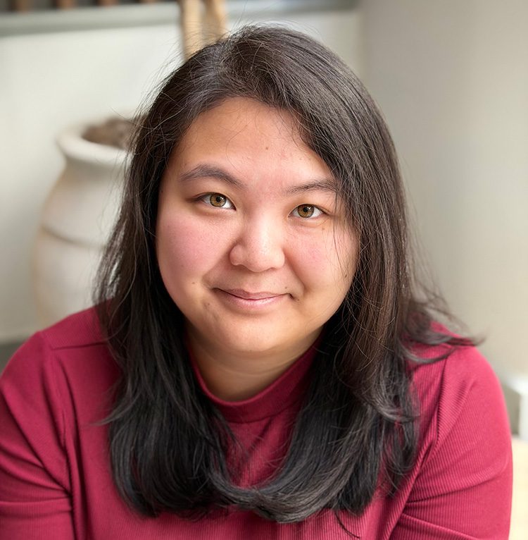 Close-up portrait of a woman with straight dark hair wearing a maroon top, smiling gently in soft natural light with a blurred background.