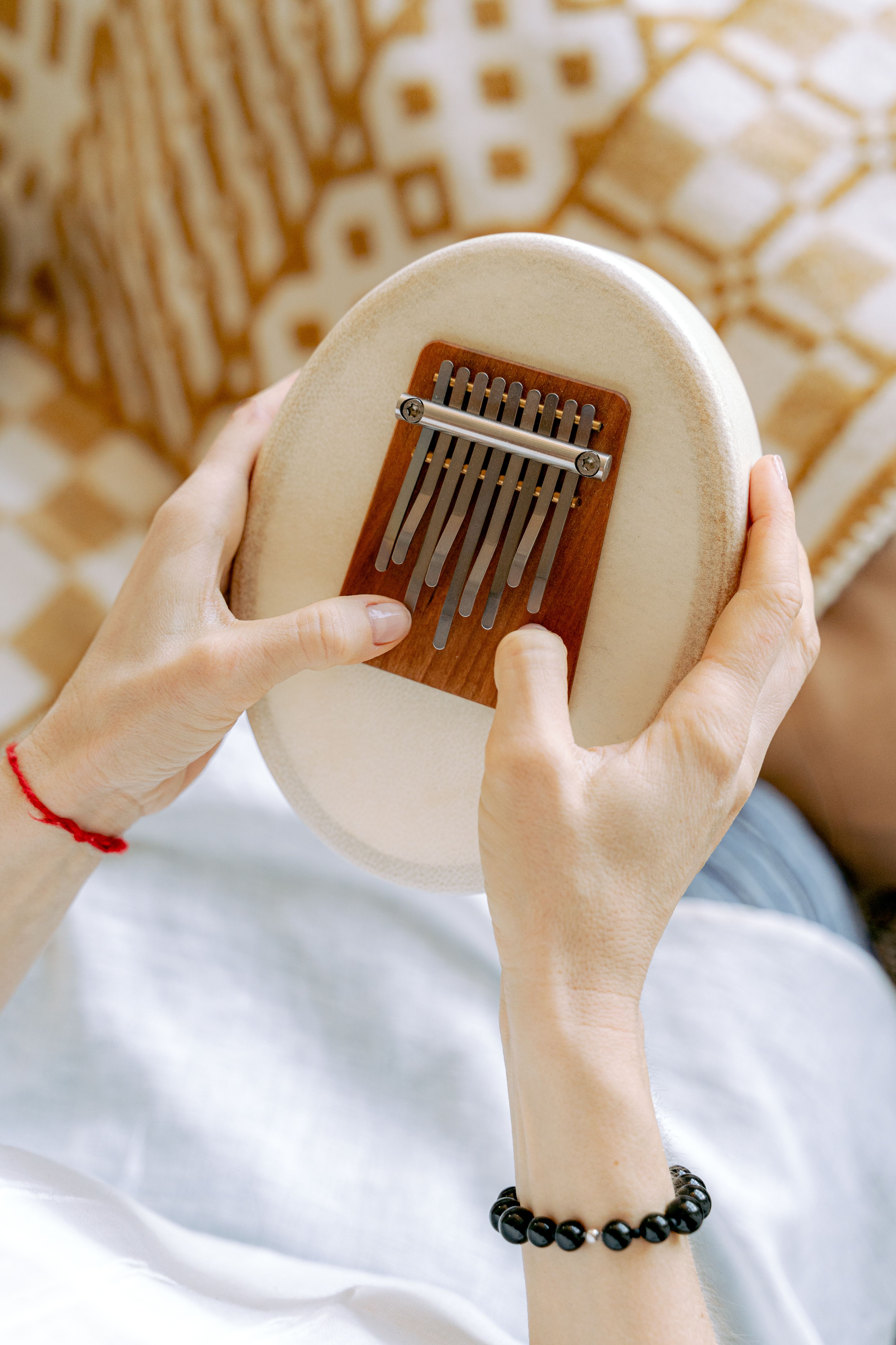 Close-up of hands playing a kalimba, a small wooden musical instrument with metal tines, against a patterned background.