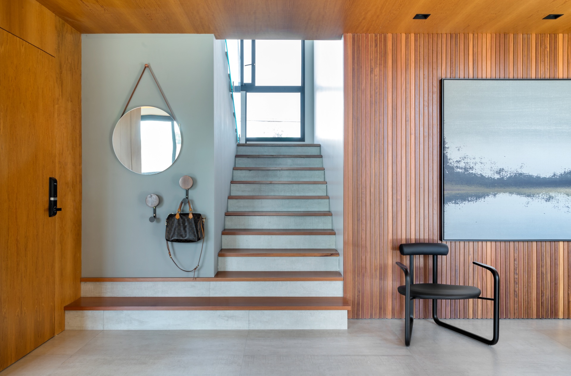 Hall de entrada contemporâneo com espelho redondo e ganchos para casacos e bolsas