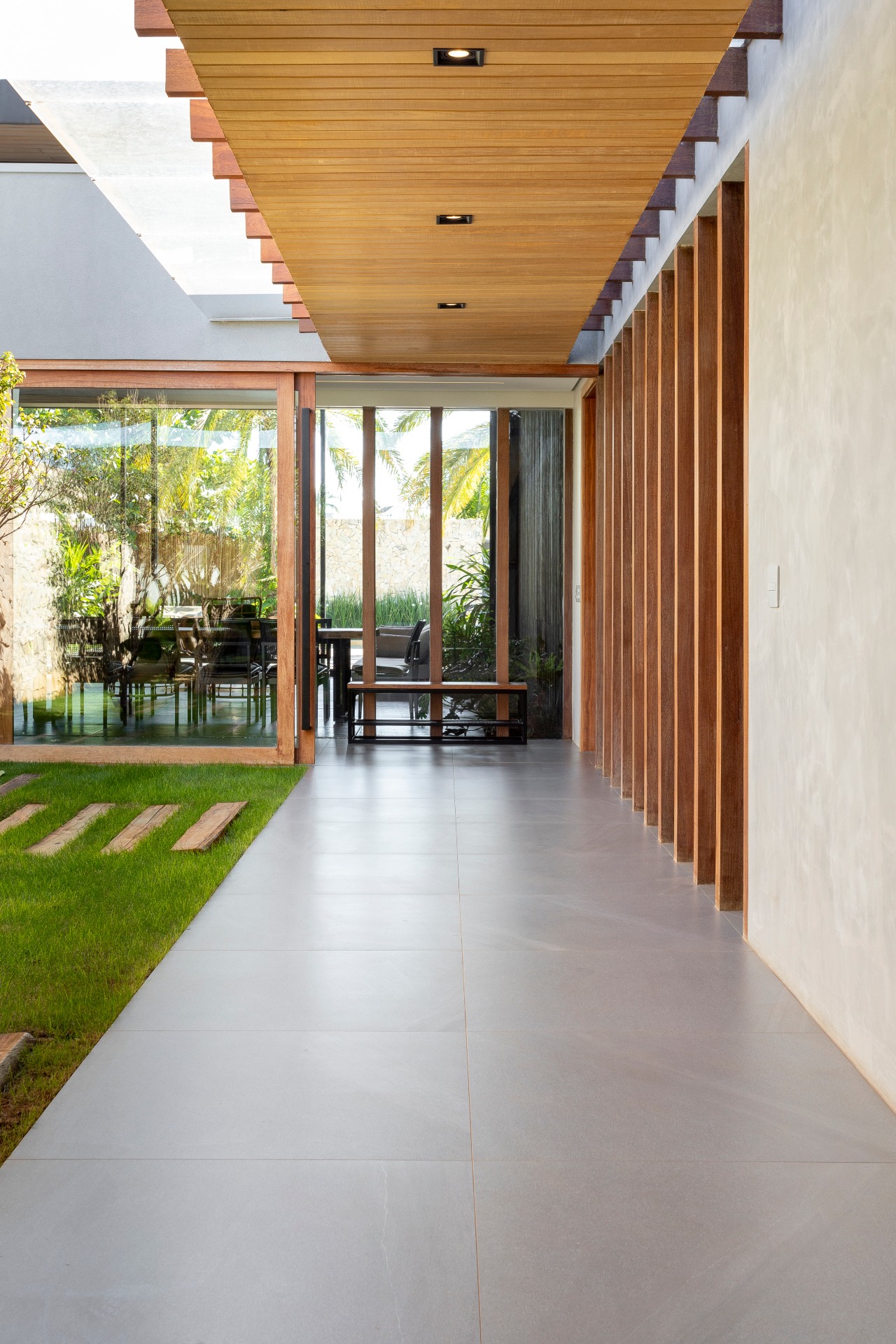 Hall de entrada externo com passagem de porcelanato que imita cimento queimado, banco metalizado e gramado