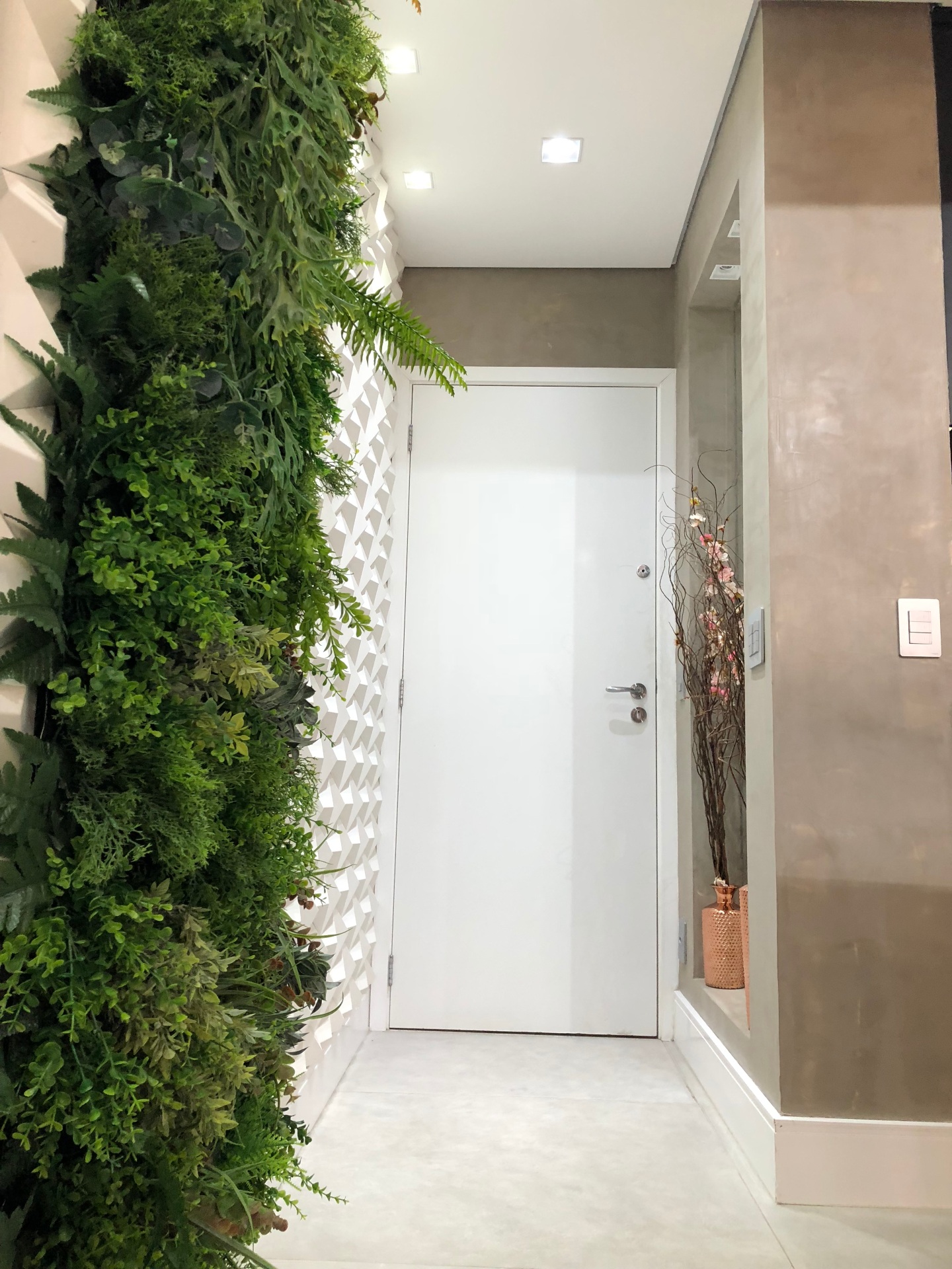 Hall de entrada pequeno com porta branca, parede branca em 3D, jarddim vertical e vasos com flores secas