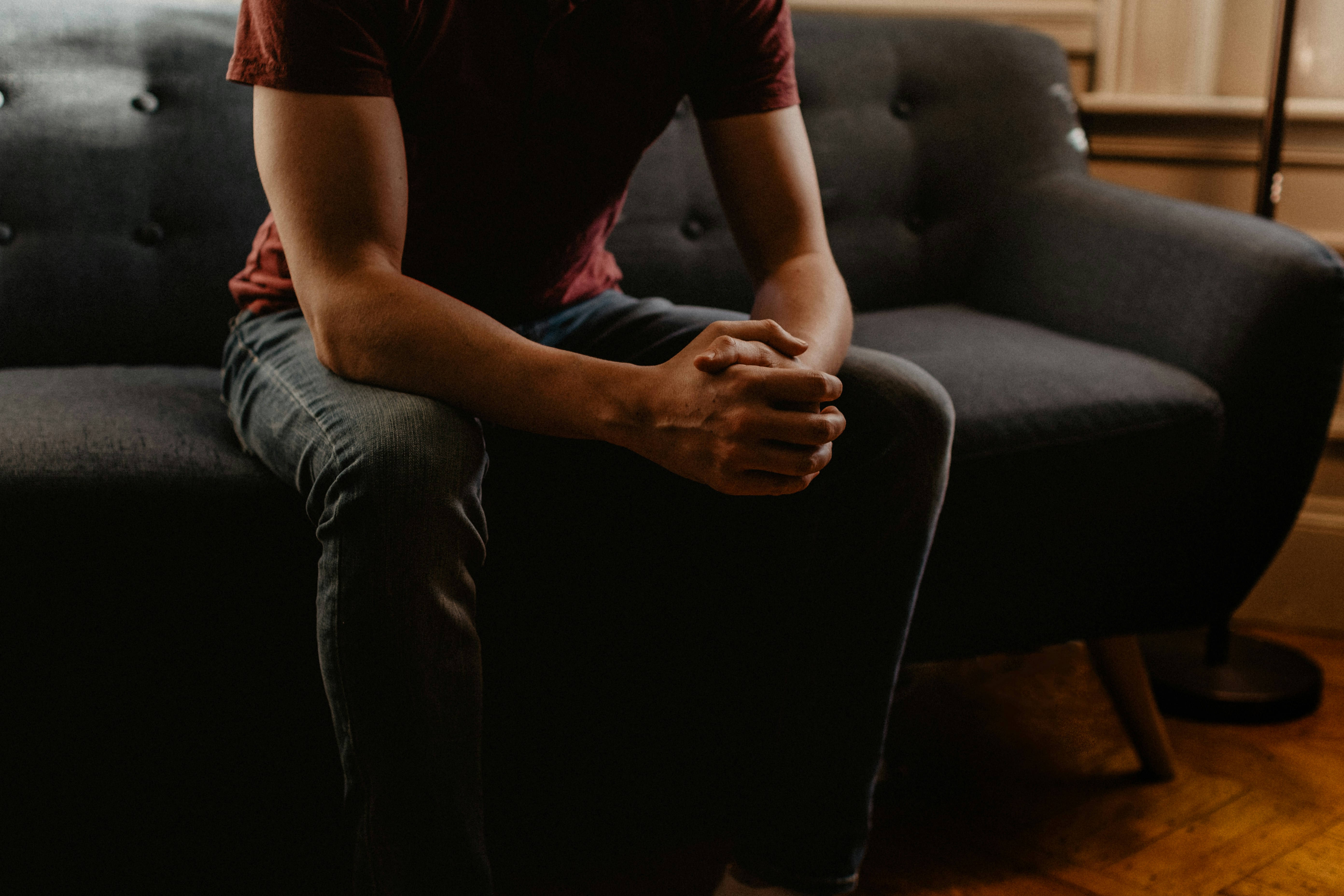 Person sitting on a couch with hands clasped, conveying a moment of reflection or emotional vulnerability—often experienced before or during therapy.