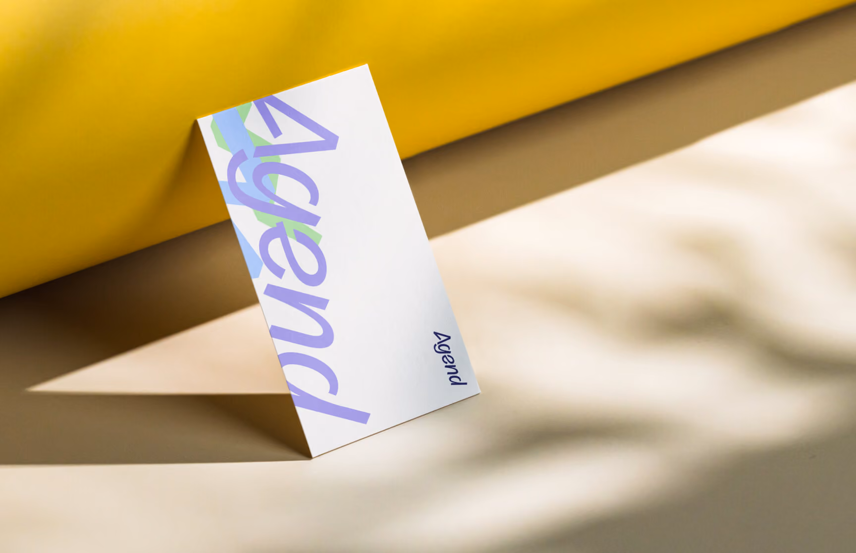 Agend business card featuring the logotype, propped up against a mustard and tan gradient backdrop.