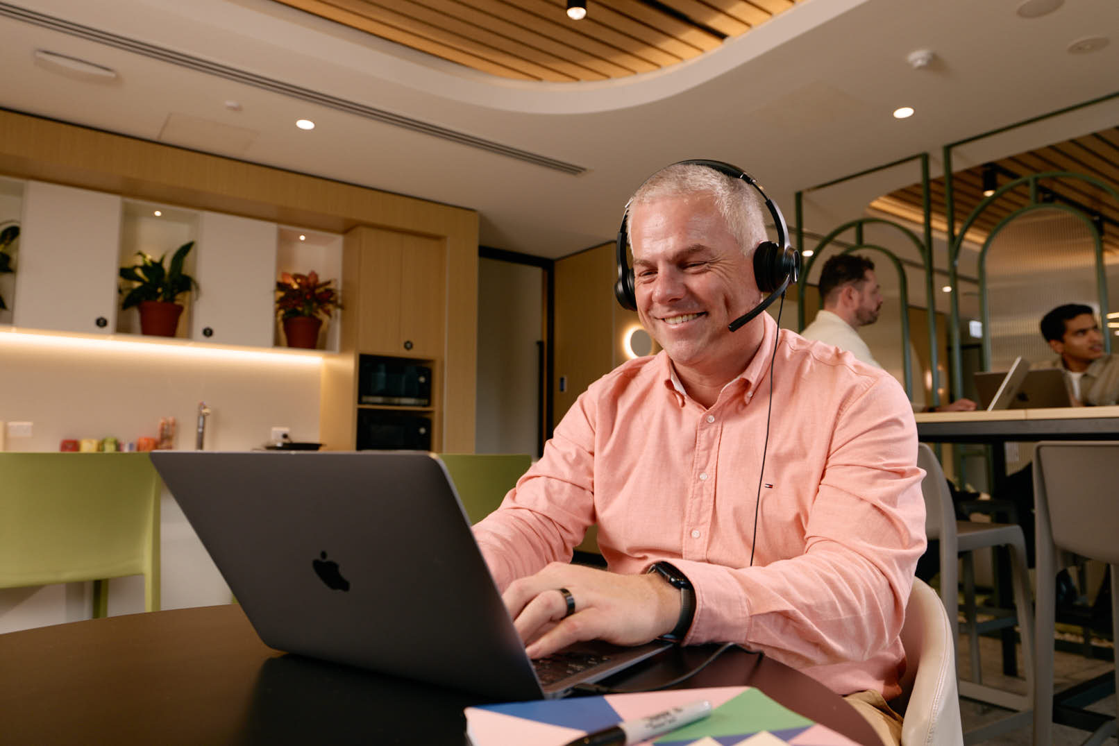 Man wearing a headset, smiling during a video call on his laptop in a bright office space, from Agend's day-in-the-life content shoot.