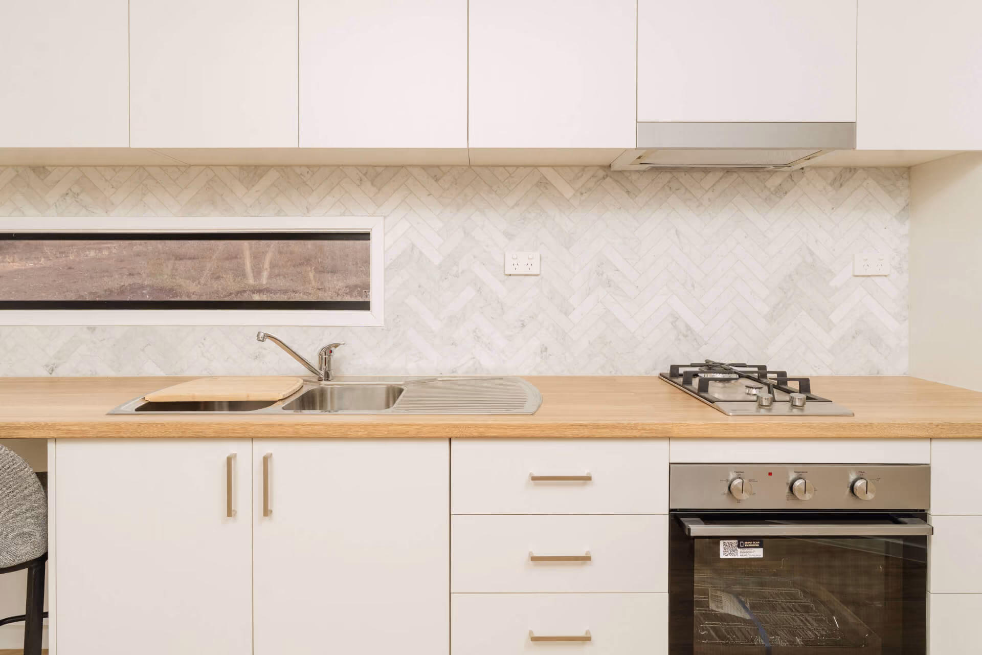 Close-up of the kitchen in a Modify home in Paradise, Adelaide, showing white cabinetry, light wooden benchtop, herringbone splashback, gas cooktop and oven.