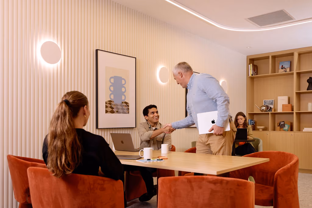 People gathered around a boardroom table with a handshake in progress, from Agend's day-in-the-life content shoot.
