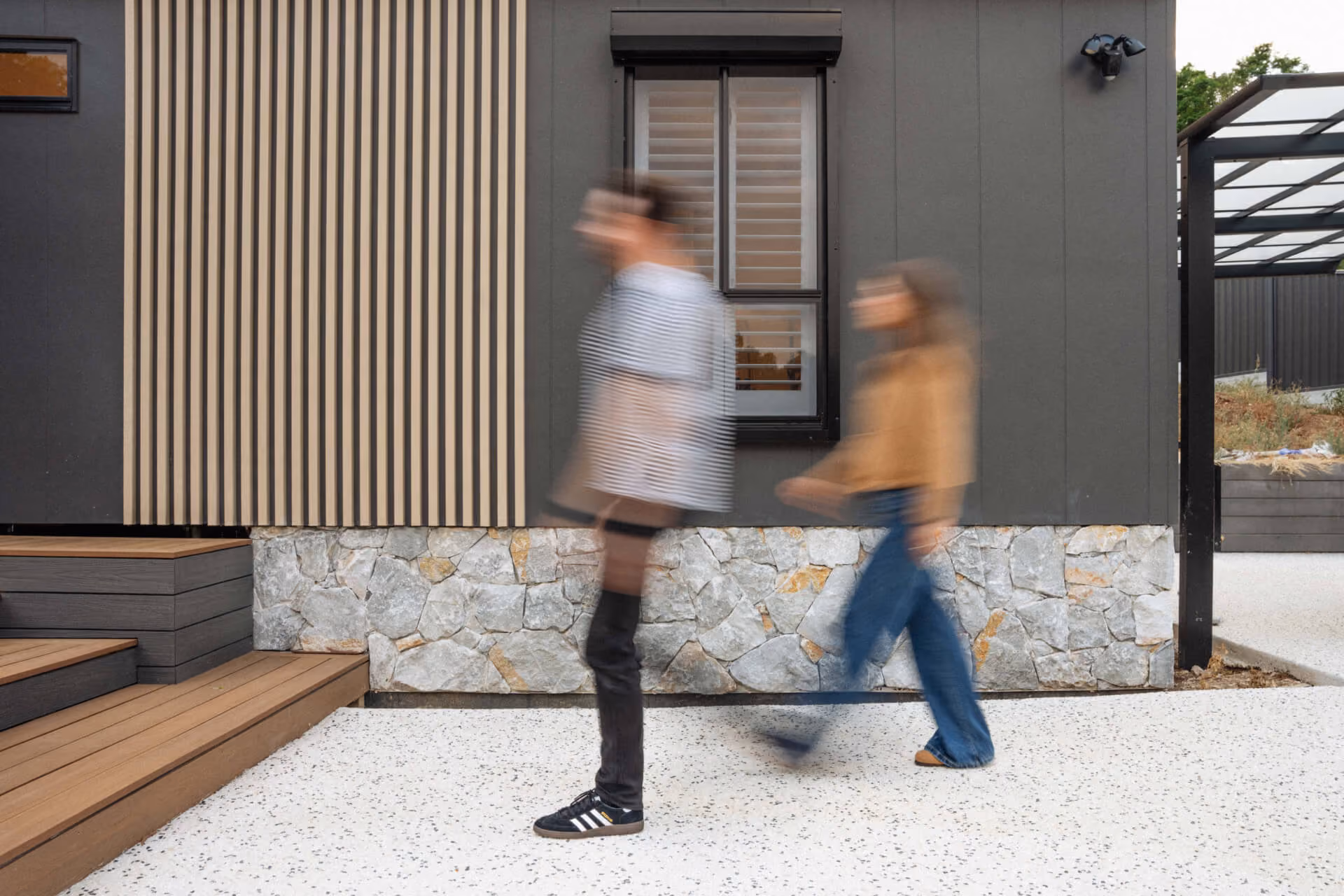 Two people walking past the front entrance of a Modify home in Paradise, Adelaide, showing the timber cladding and stone facade.