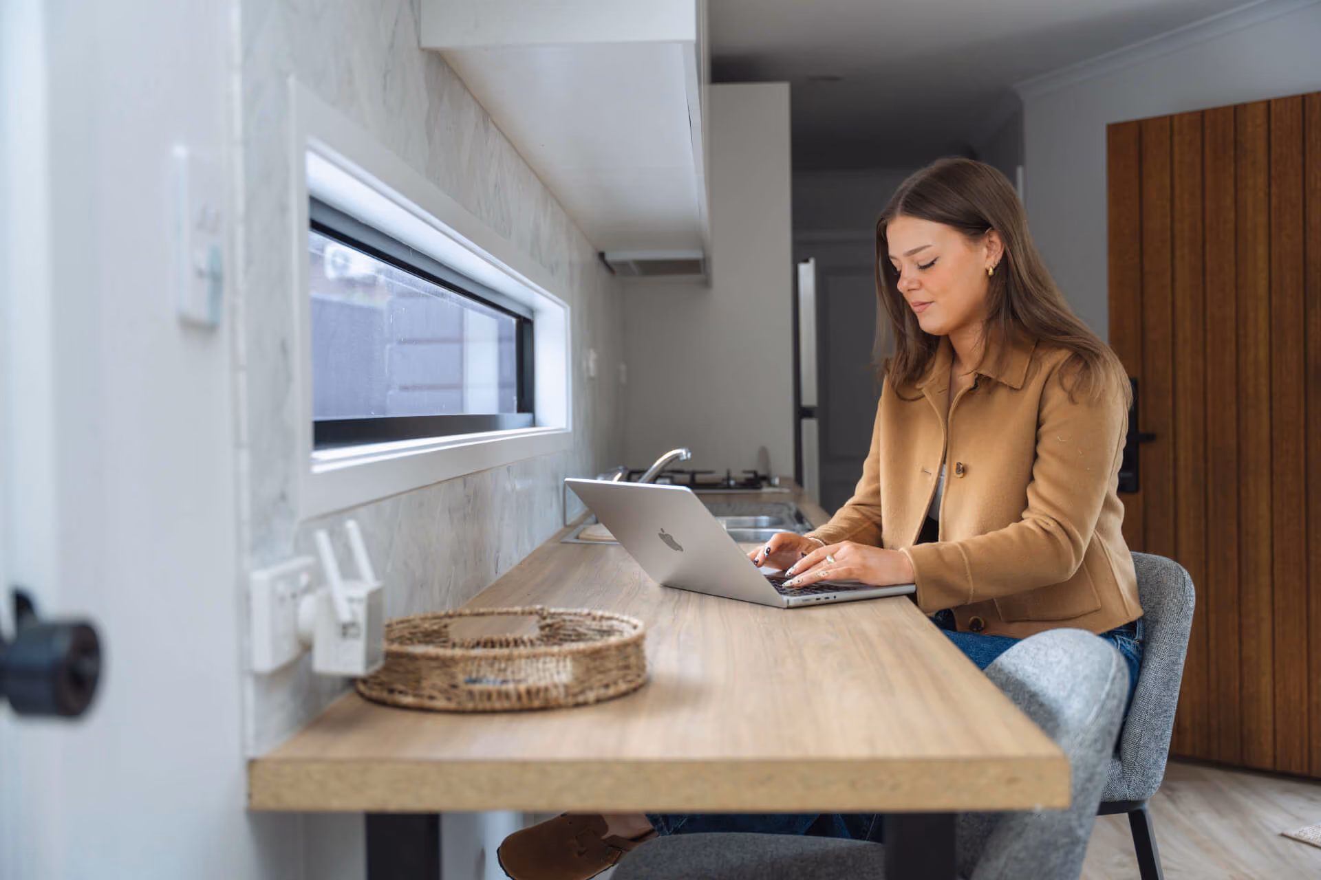 Woman working on a laptop at a timber kitchen bench inside a Modify home in Paradise, Adelaide.