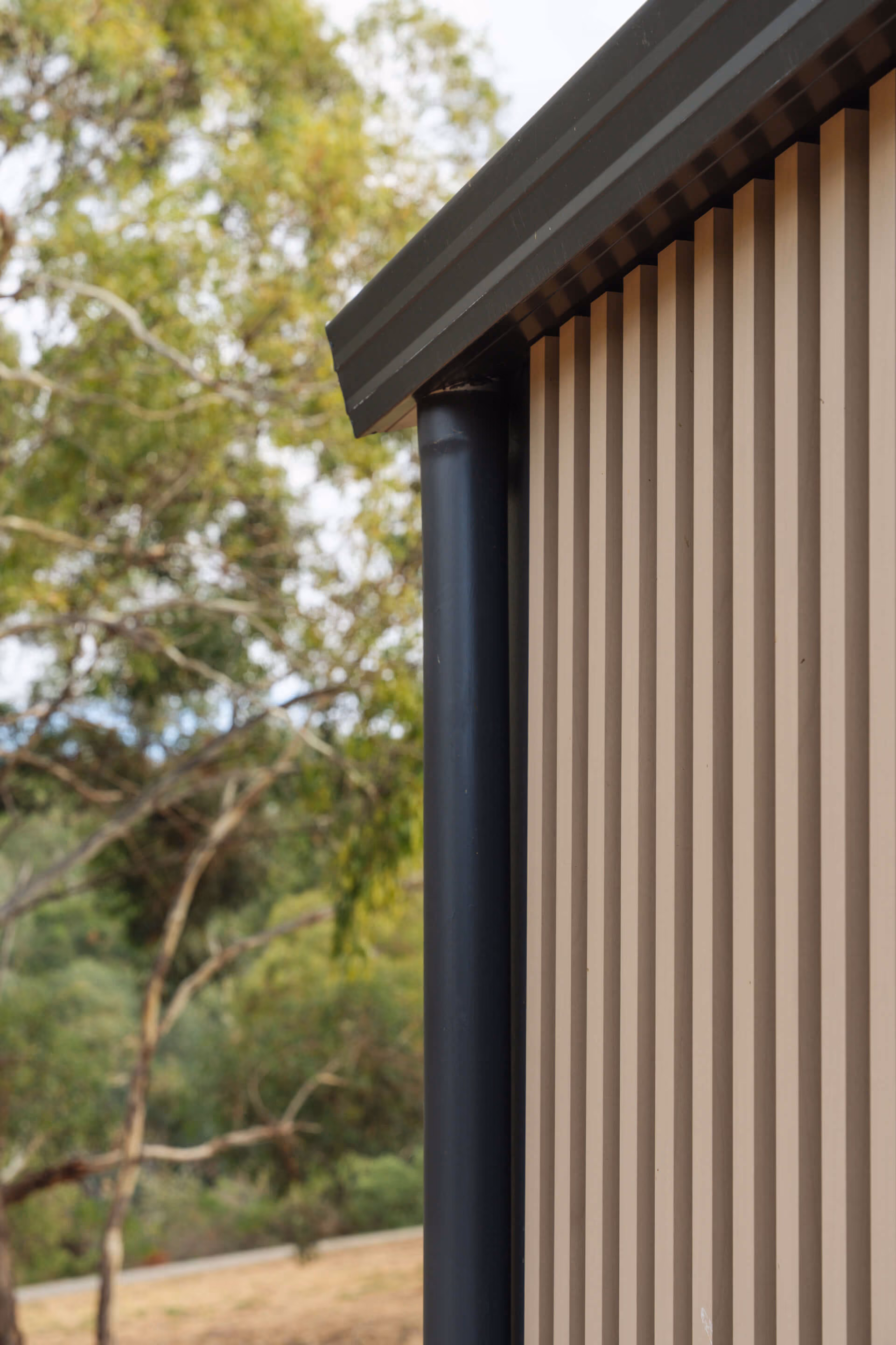 Close-up of the vertical steel cladding and roofline detail on a prefab house, with trees in the background.