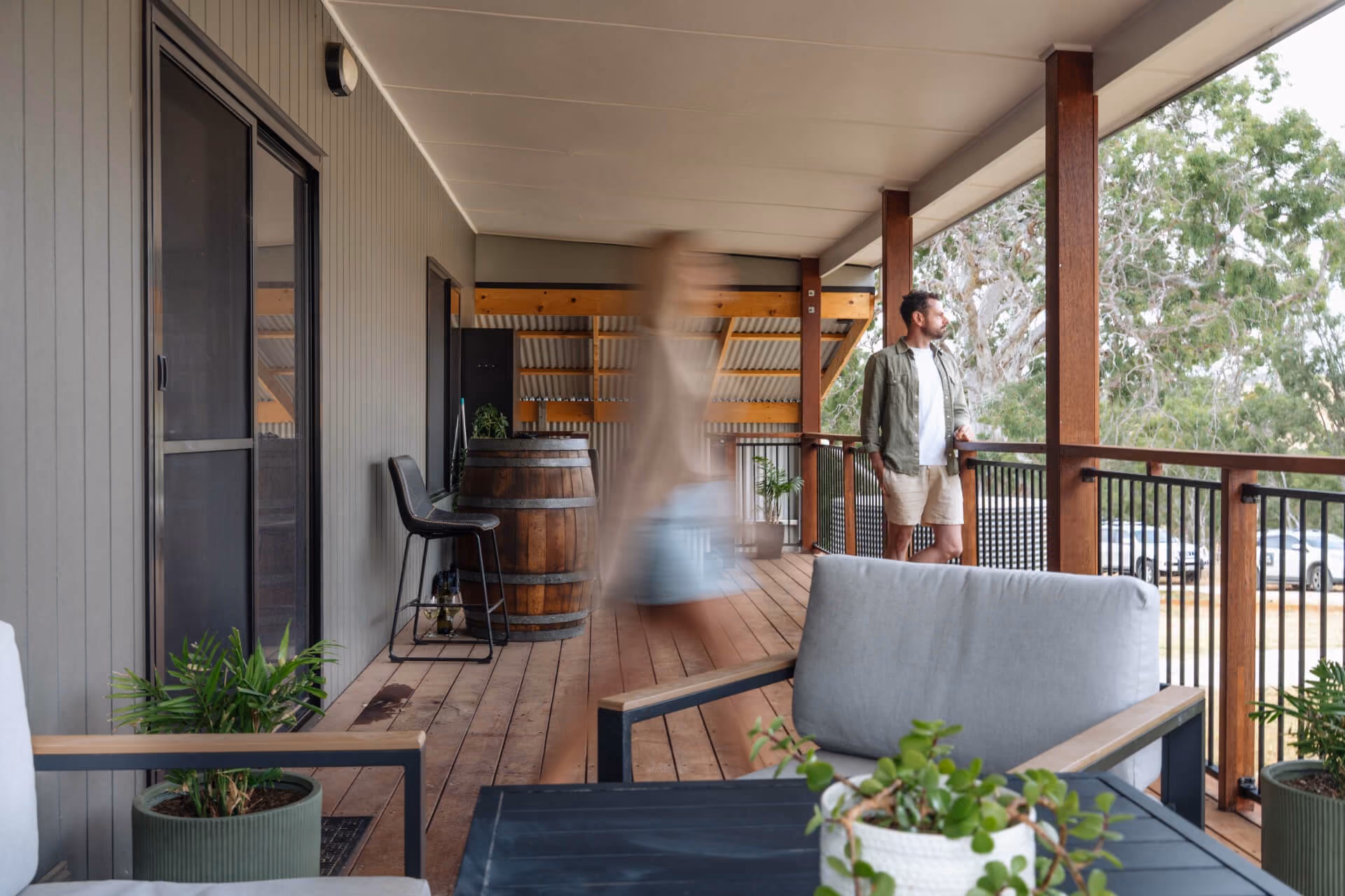 Man standing on a timber veranda while another person moves past in motion, part of the Modify Adelaide Hills prefab home's outdoor living space.