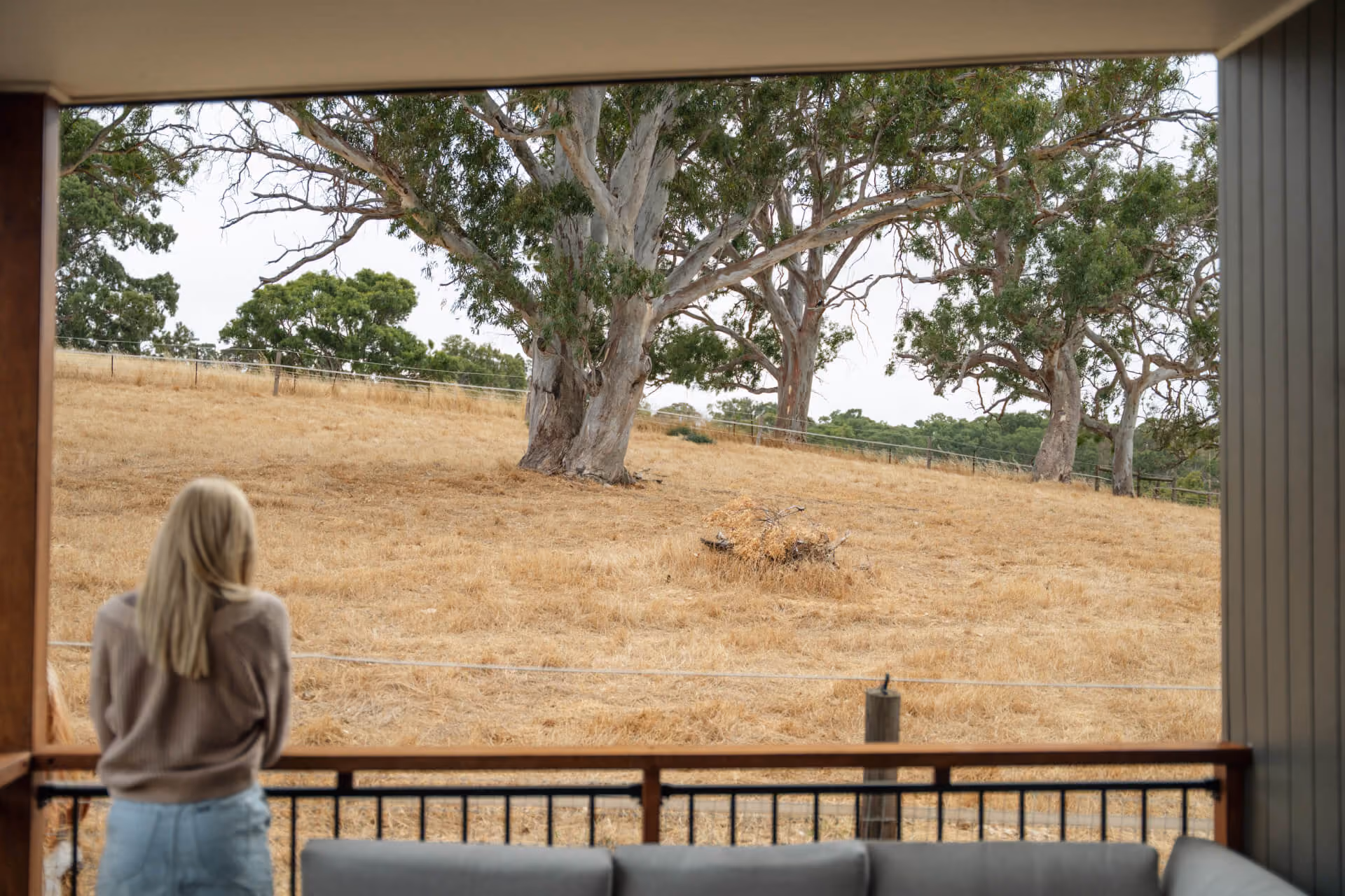 Woman standing on a covered veranda looking out over open paddocks and gum trees at an Adelaide Hills Modify modular home.