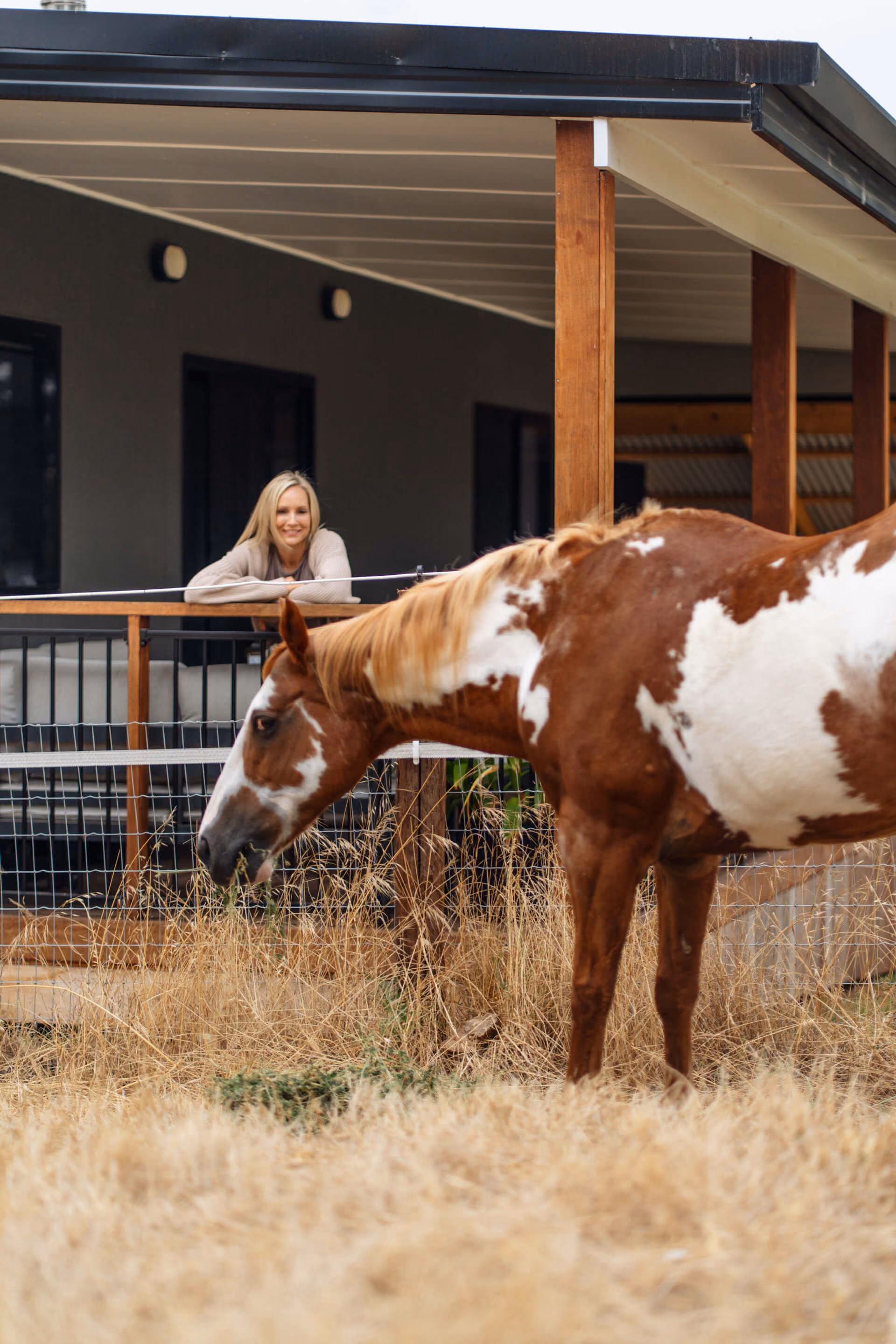 Woman standing outside a modern home with a brown and white horse in the Adelaide Hills