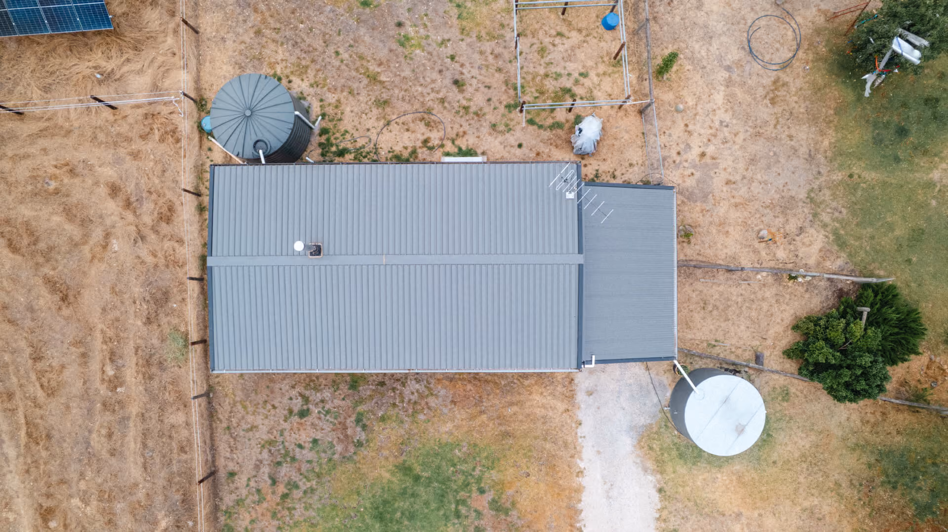 Aerial drone view of a large grey modular home on a rural Adelaide Hills property, surrounded by open land and scattered trees.