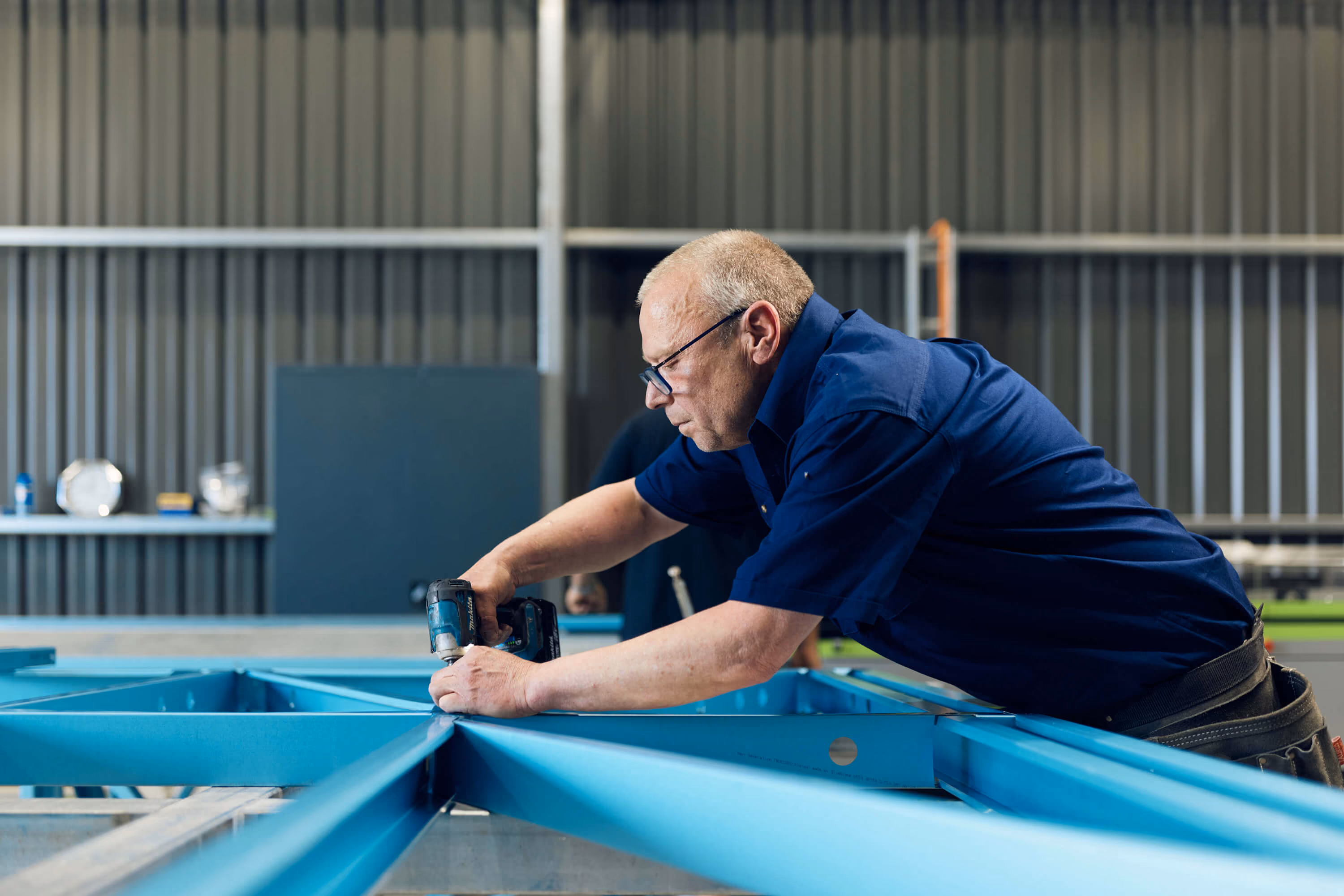 Modify Steel worker assembling a blue steel frame with a drill in the workshop.
