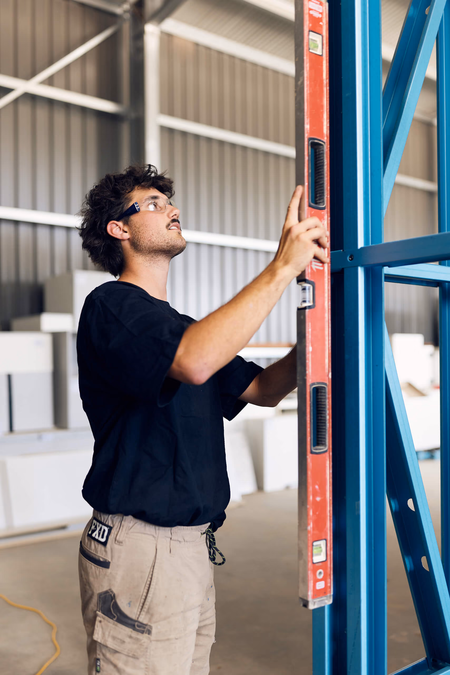 Modify Steel worker checking a blue steel frame with a spirit level in a workshop. 