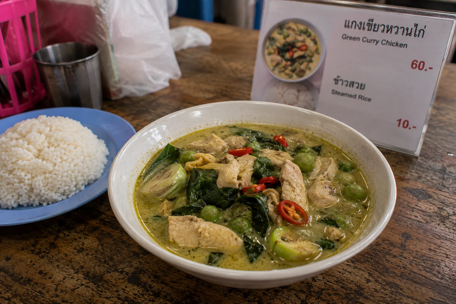 A bowl of Thai green curry with chicken, Thai basil, pea aubergines and red chilli, served with steamed rice at a Thai food stall