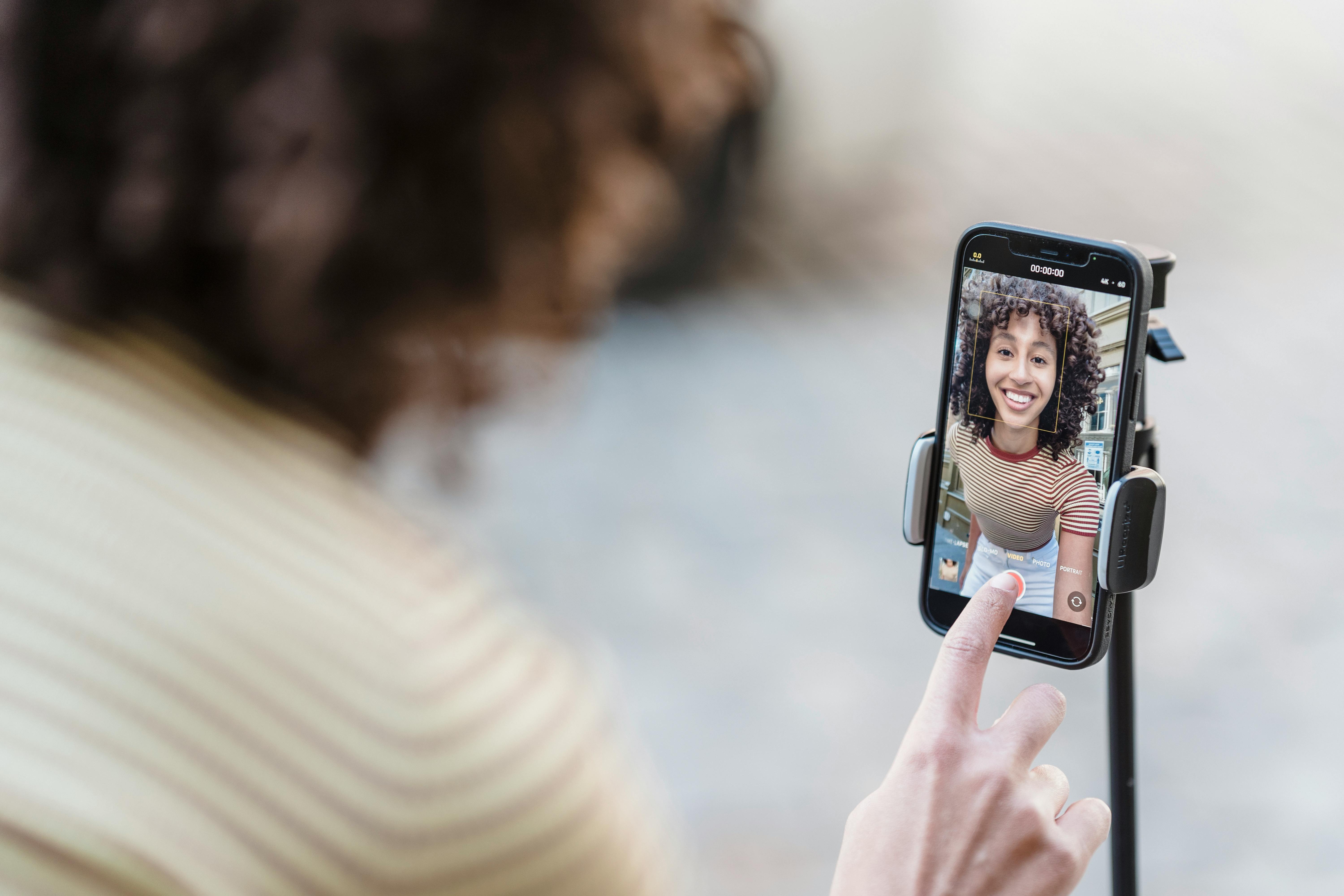 young influencer woman pressing record on an iphone while smiling into camera