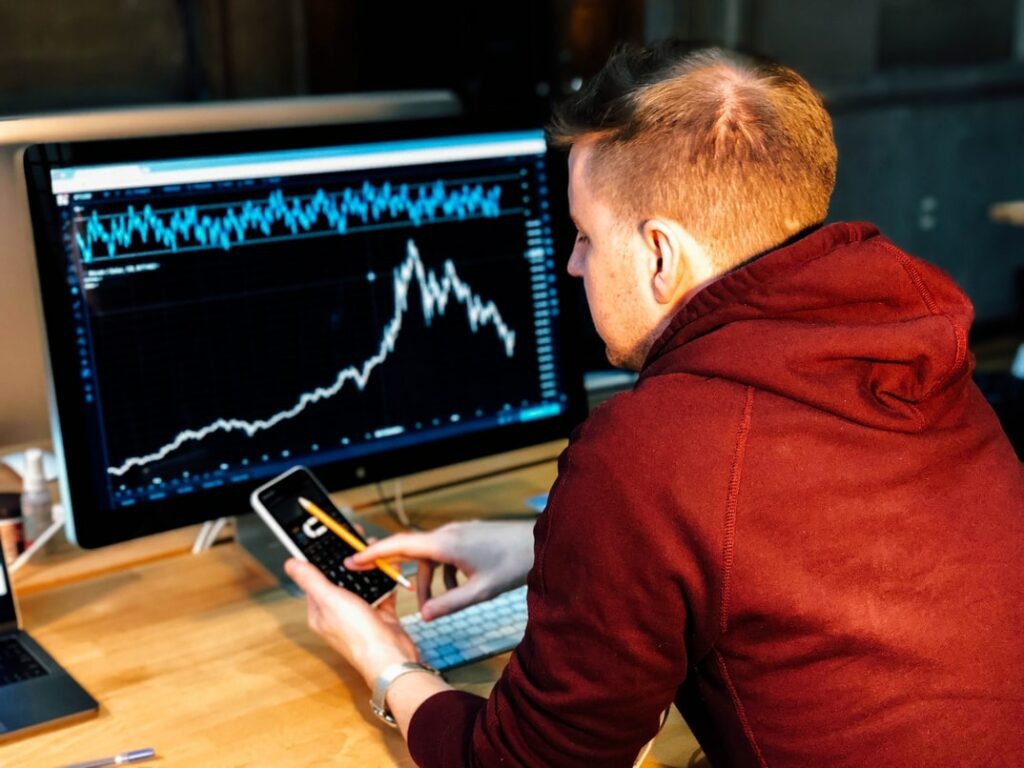 Man in red hoodie sitting in front of computer screen with analytics graph