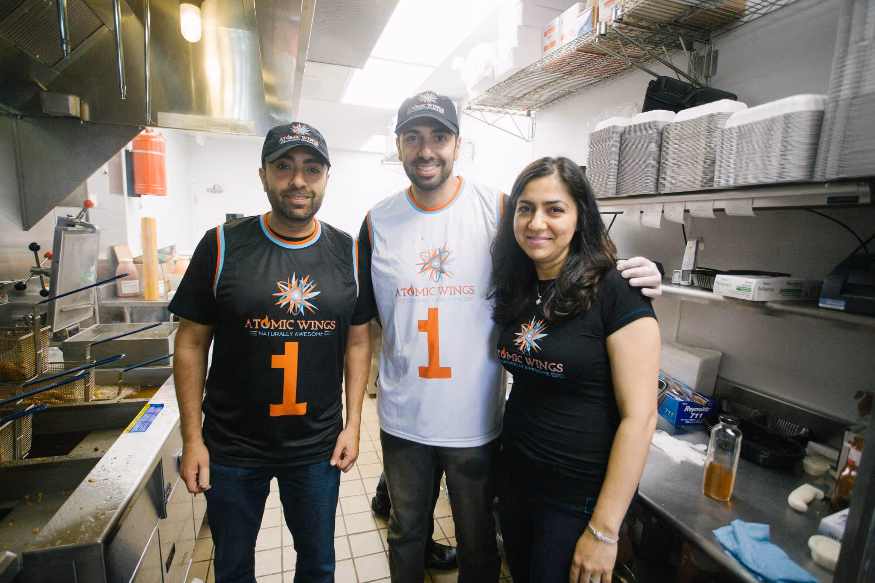 Three people standing together for a picture in the kitchen of an Atomic Wings