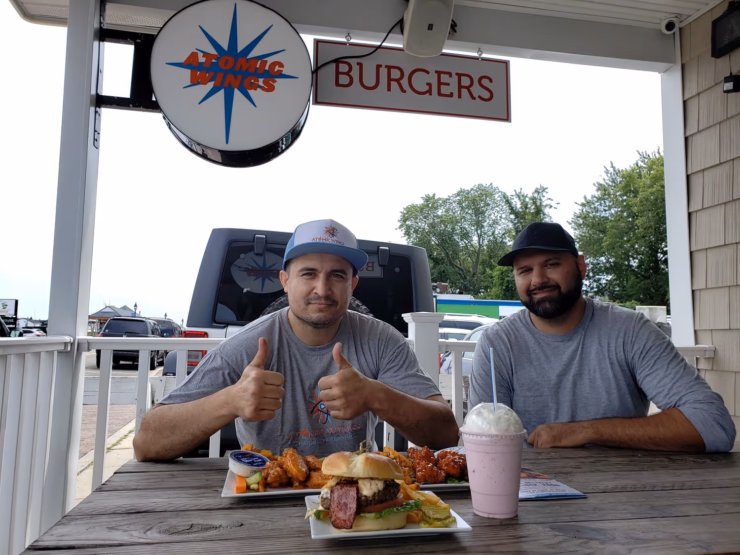 two men, one holding thumbs up, eating at an atomic wings restaurant