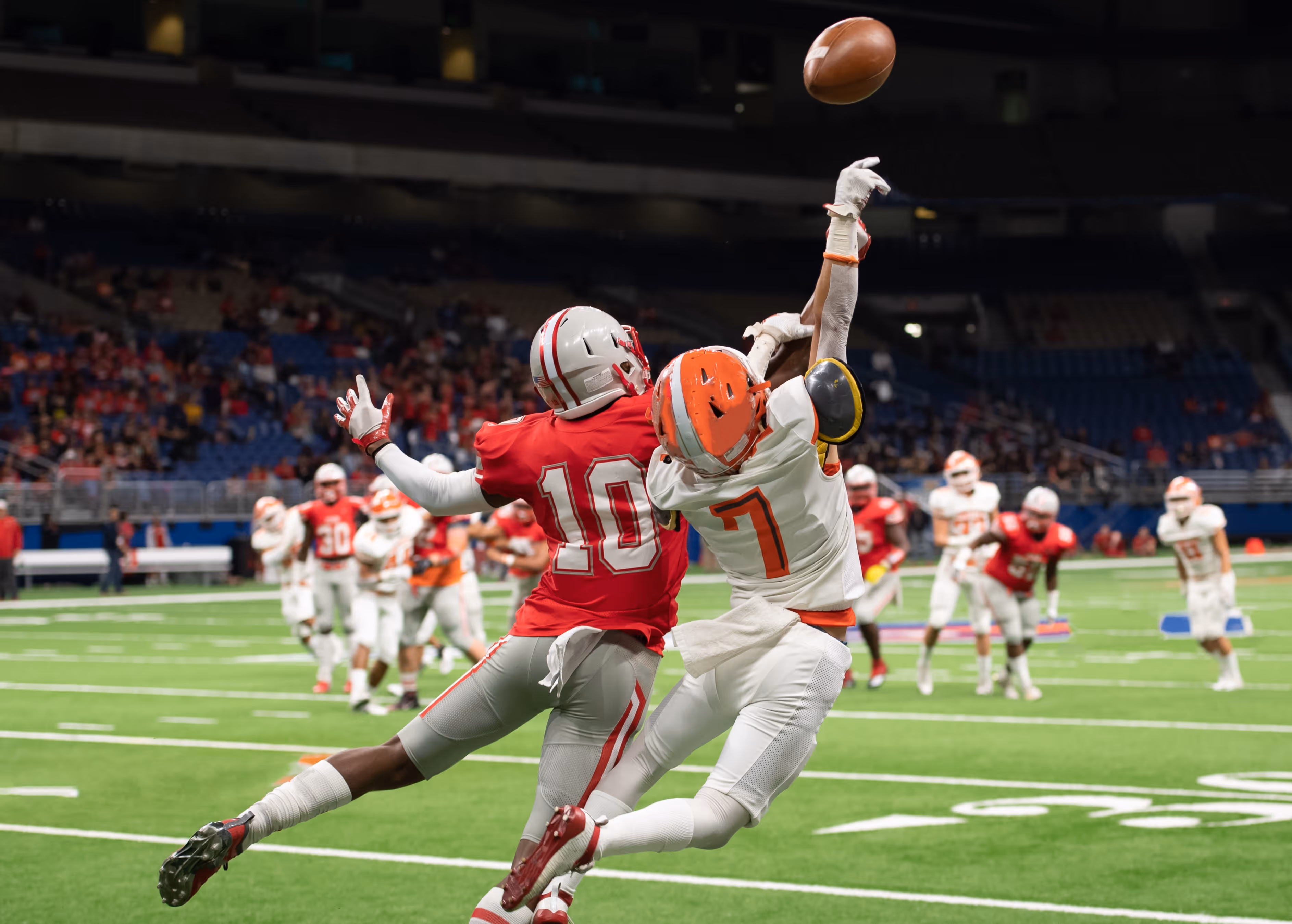 American football wide receiver and cornerback contest for the ball in a football game