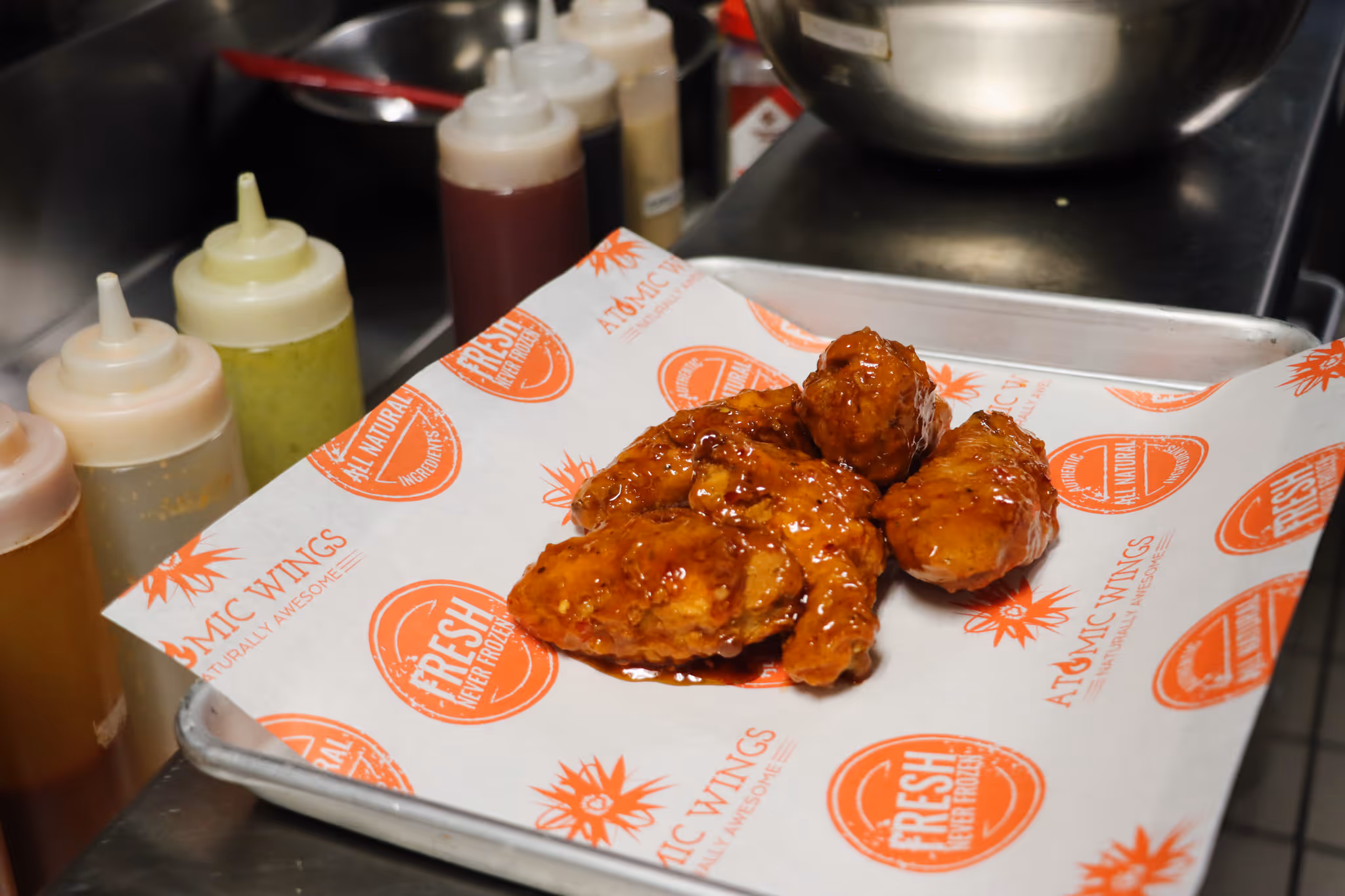 A plate of wings from Atomic Wings with different wing sauces in the background