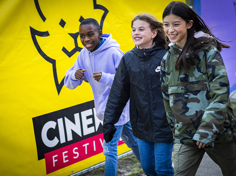 Promotional photo from Cinekid, with three kids walking past a wall with a Cinekid logo on it