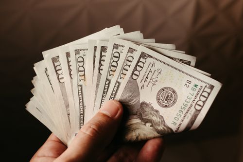 Mano sosteniendo varios billetes de 100 dólares en abanico, imagen relacionada con delitos económicos.