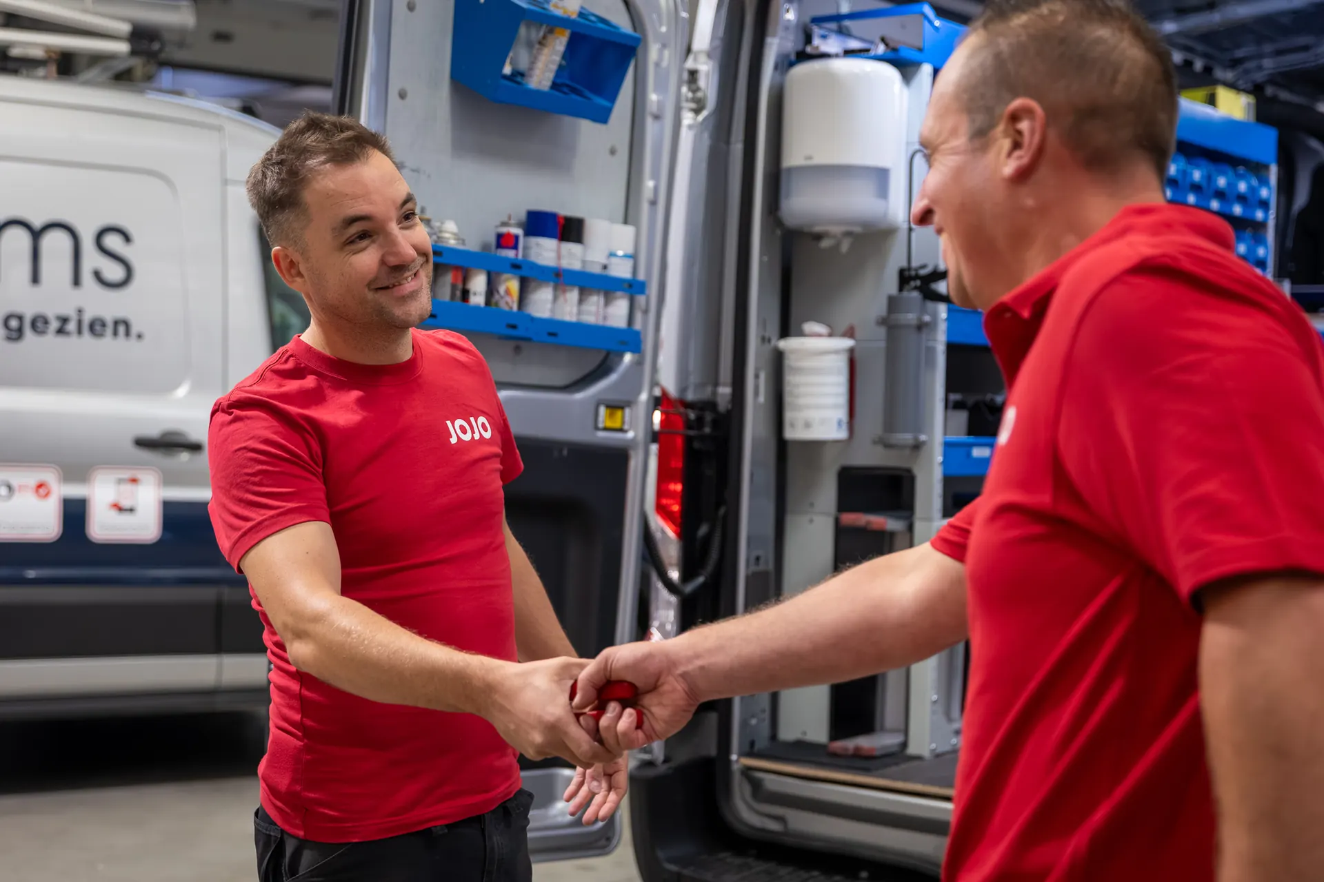 Twee technici van JOJO Systems geven elkaar een hand bij de servicewagen