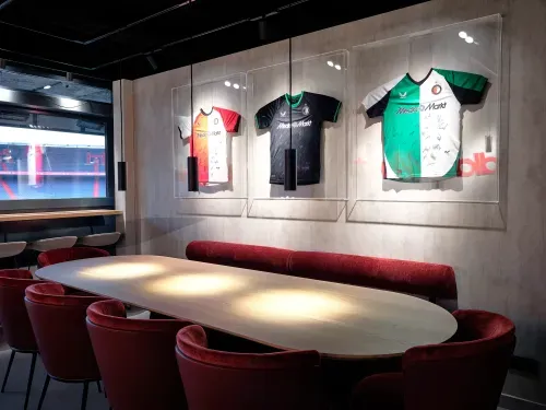 Modern conference room with a wooden oval table, red velvet chairs, and three signed football jerseys displayed on the wall.
