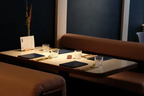 Restaurant table set for four with glasses, gold cutlery, menus. Materials include Querkus MDF