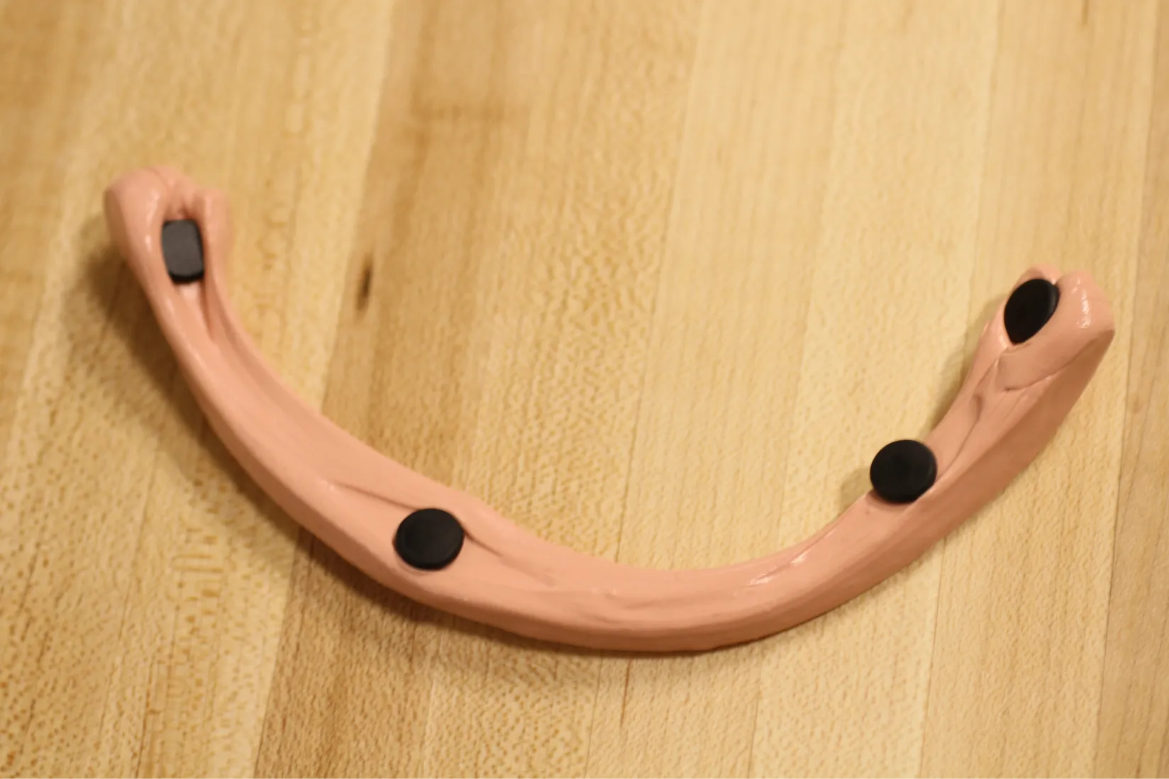 Stretch-curved clay toy prototype with embedded black RFID tags placed on a wooden surface.