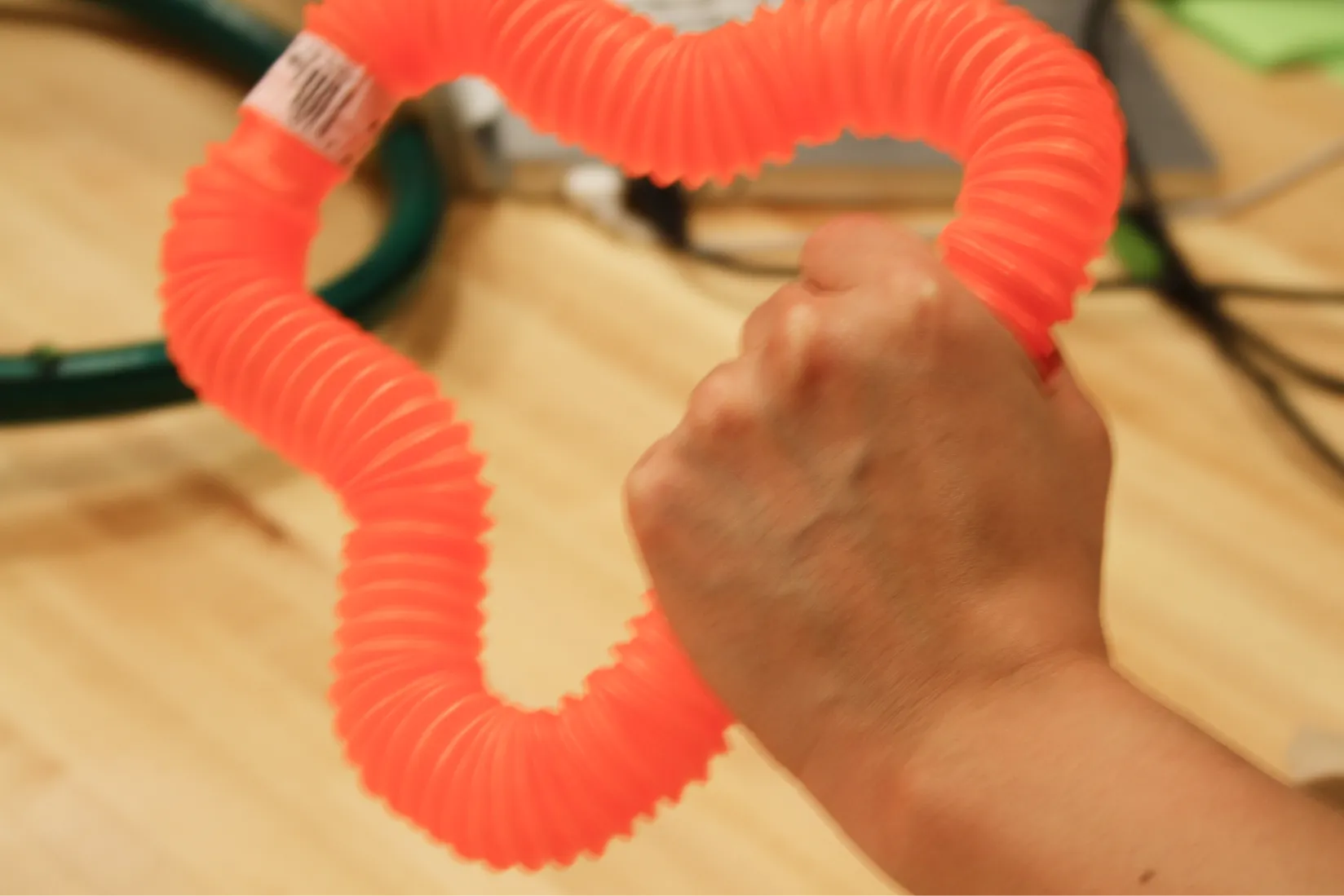 Hand holding a flexible toy prototype made from an orange corrugated plastic tube.