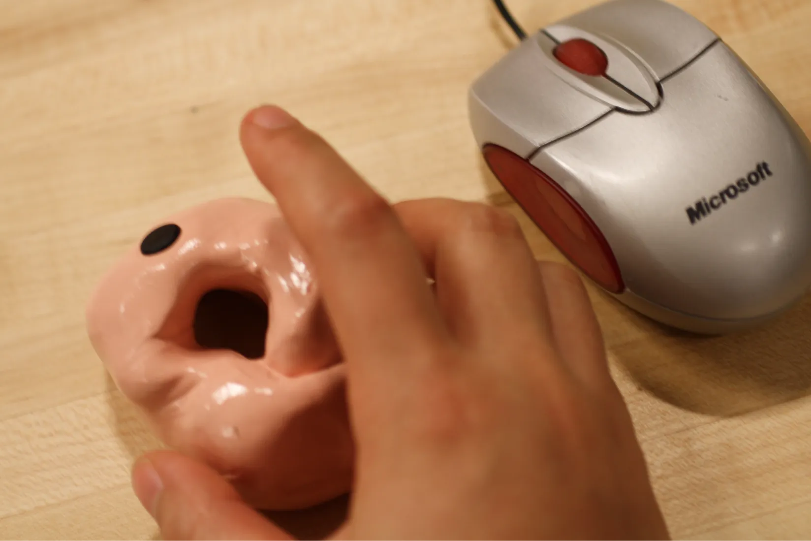 A hand holding a round lump of clay with an RFID like holding a computer mouse, and an actual mouse next to it.