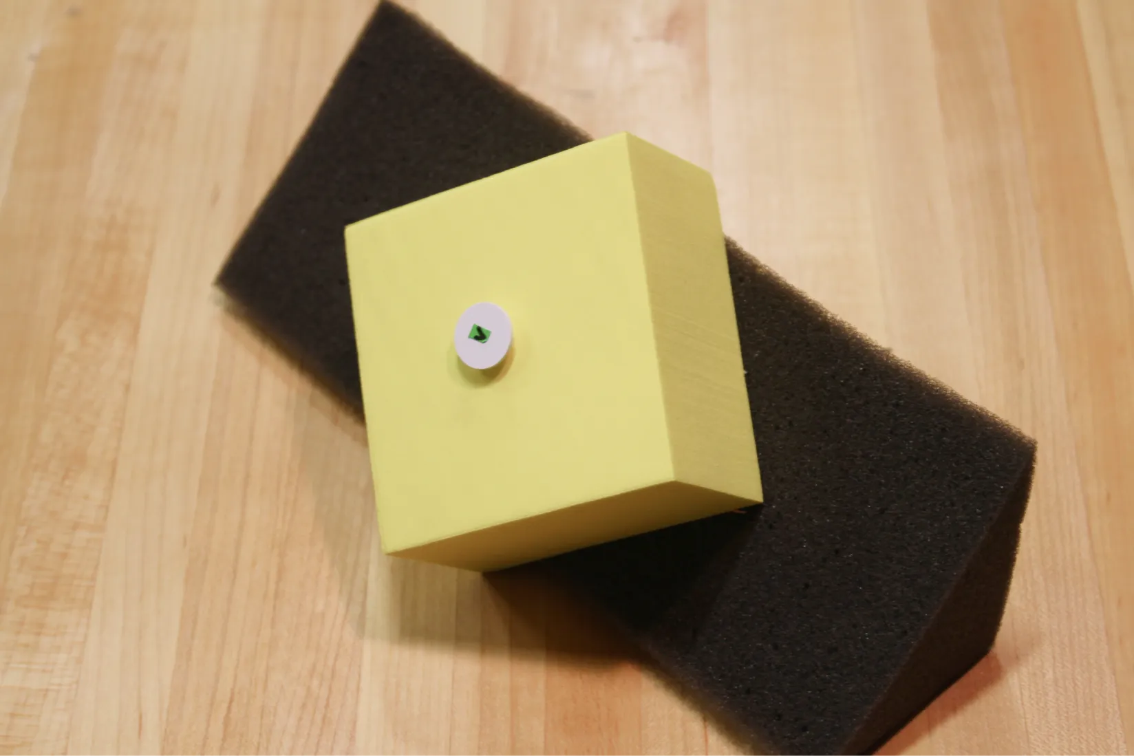 Foam squeezy toy prototype with a small RFID tag attached to a yellow sponge on top of a black sponge base.