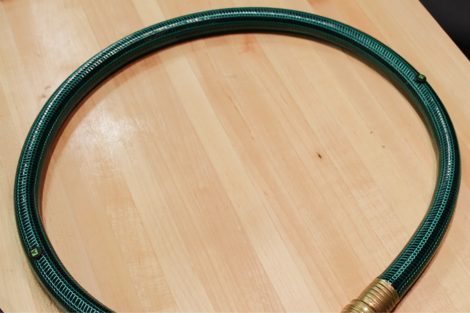 Circular loop toy prototype made from a flexible green hose placed on a wooden surface. Two small RFID tags are seen glued on the loop.