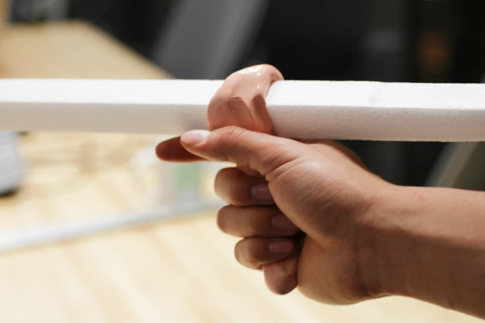 Hand gripping a band of clay wrapping around a straight white rod toy prototype used for pointing or triggering interaction.