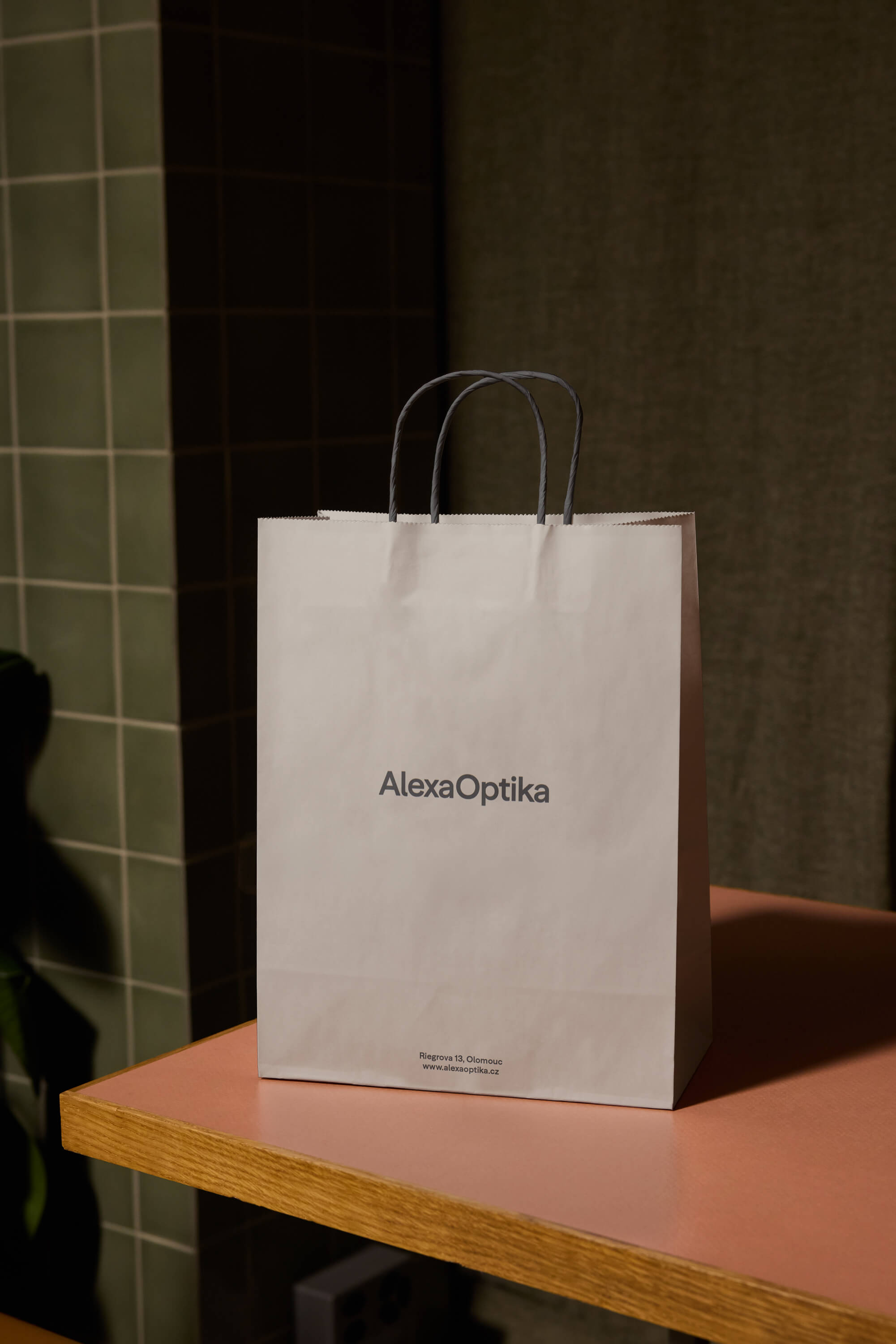 Papírová taška Alexa Optika s minimalistickým logem a adresou provozovny v Olomouci.