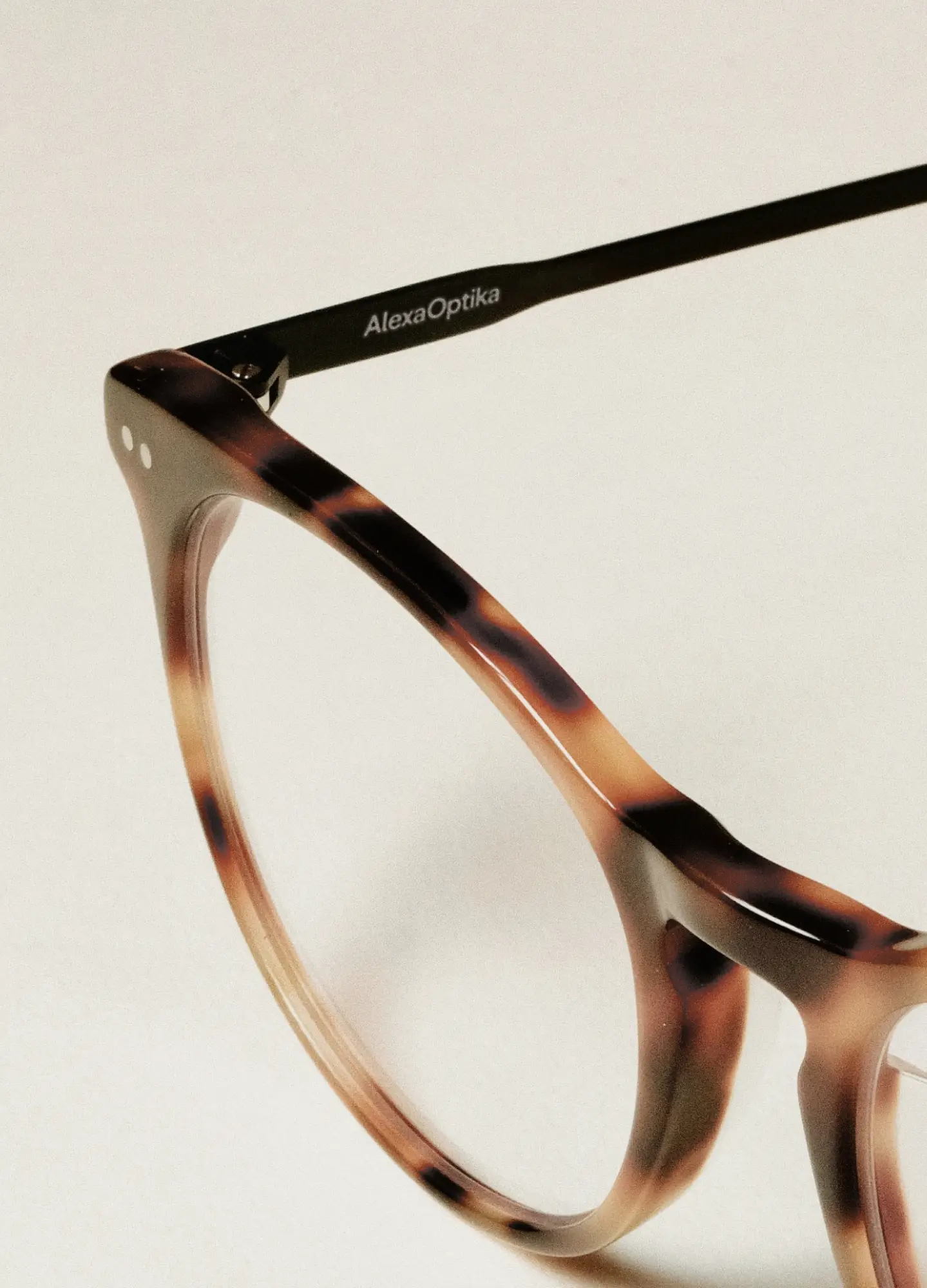 Detail hnědých brýlových obrub s logem Alexa Optika na nožičce, elegantní produktová fotografie.