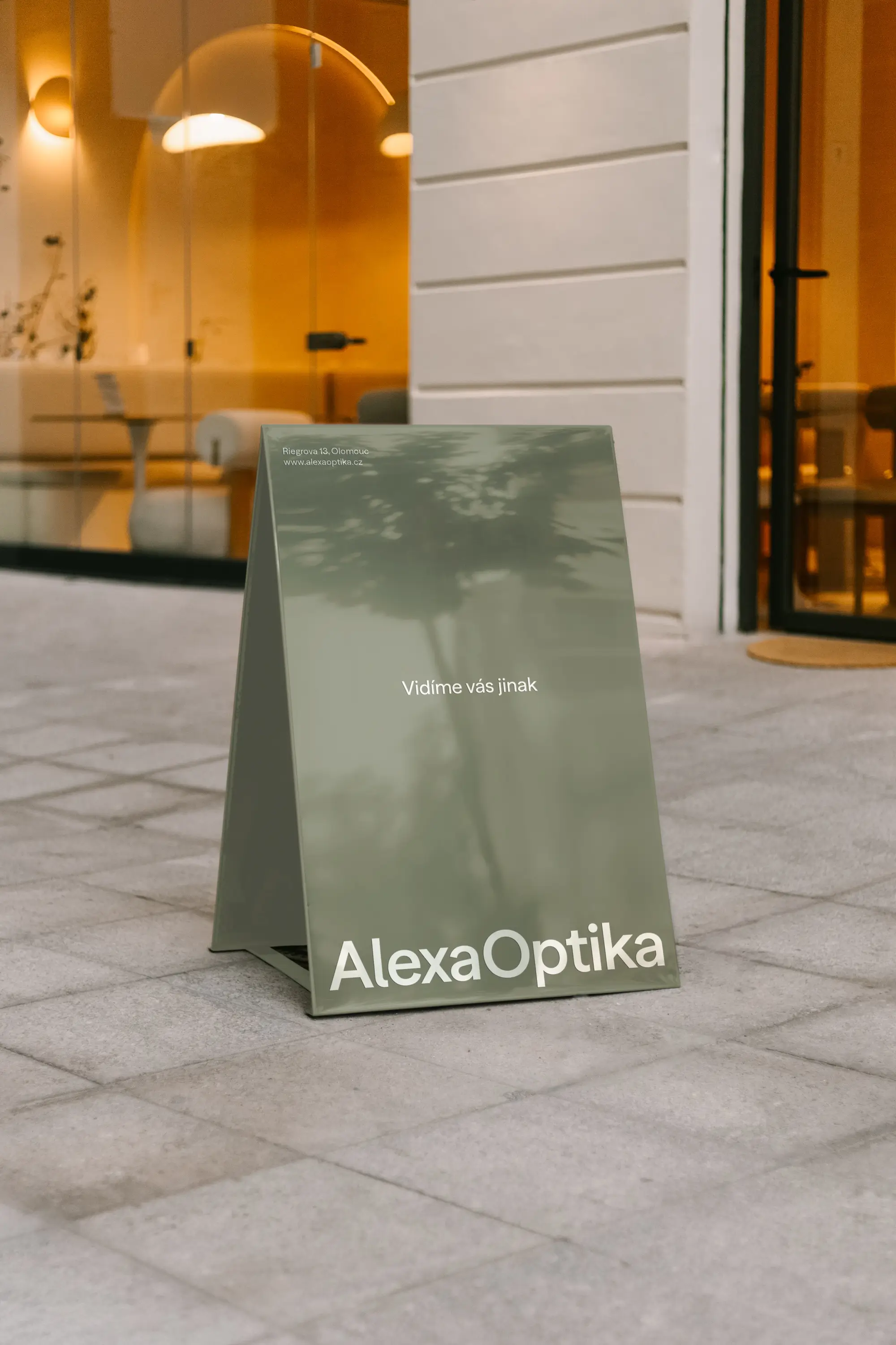 Před provozovnou Alexa Optika stojí elegantní oboustranné áčko s nápisem „Vidíme vás jinak“.