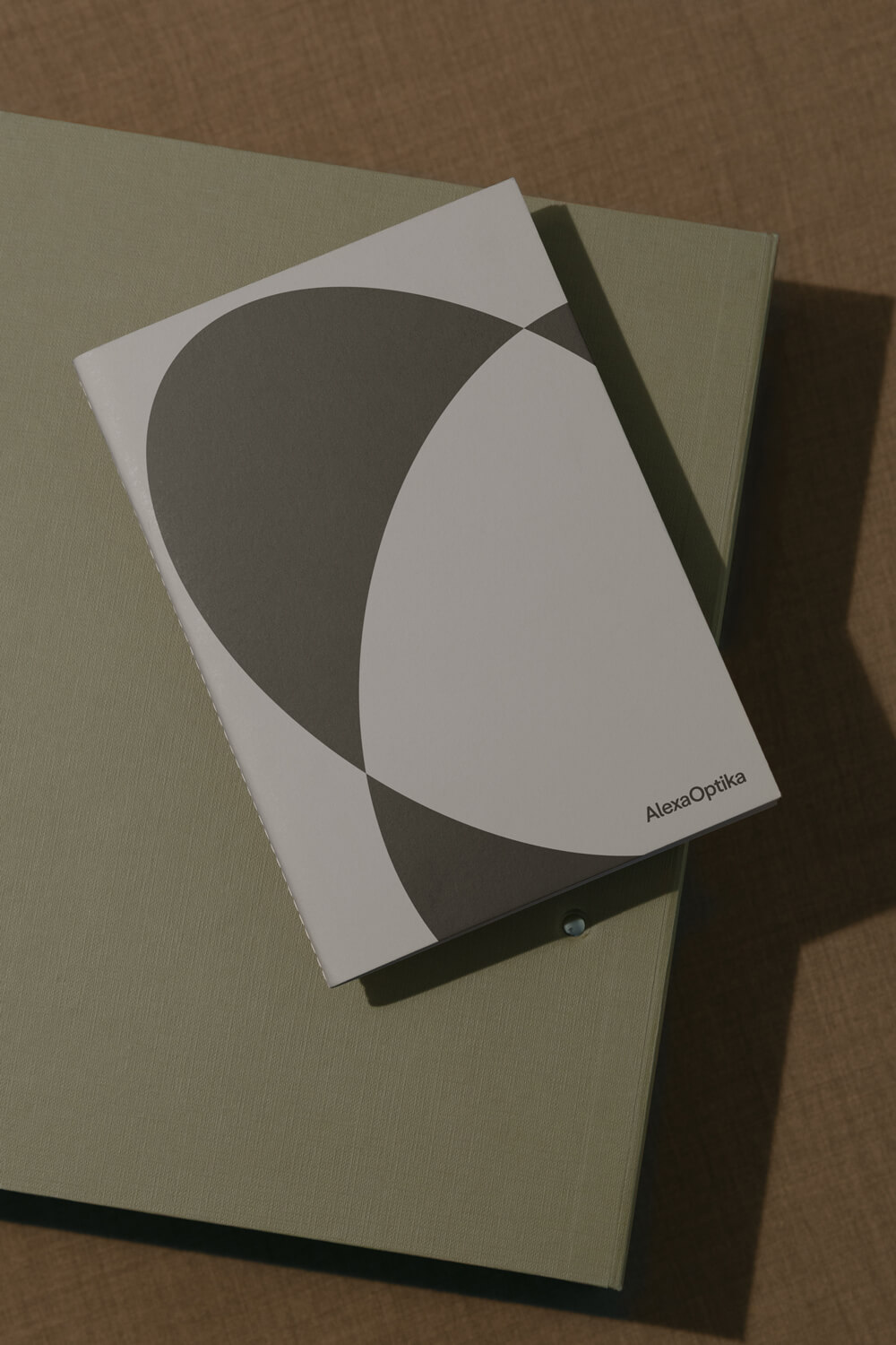 Tištěný sešit Alexa Optika s minimalistickým geometrickým motivem v odstínech šedé a olivové.