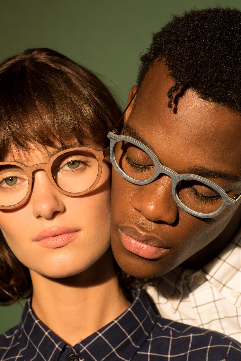 Detailní portrét dvojice s brýlemi Alexa Optika, v teplém světle s kontrastním zeleným pozadím.