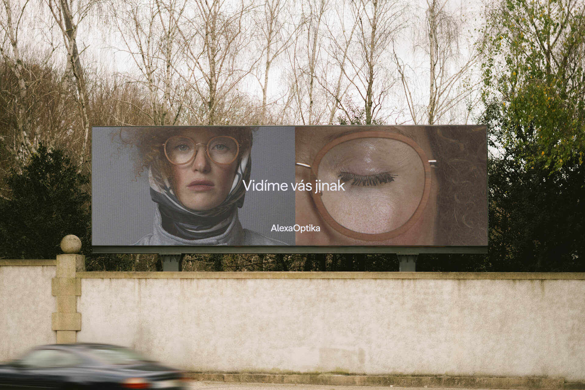 Billboard s kampaní Alexa Optika „Vidíme vás jinak“ s portrétem ženy v brýlích a detailem zavřeného oka.