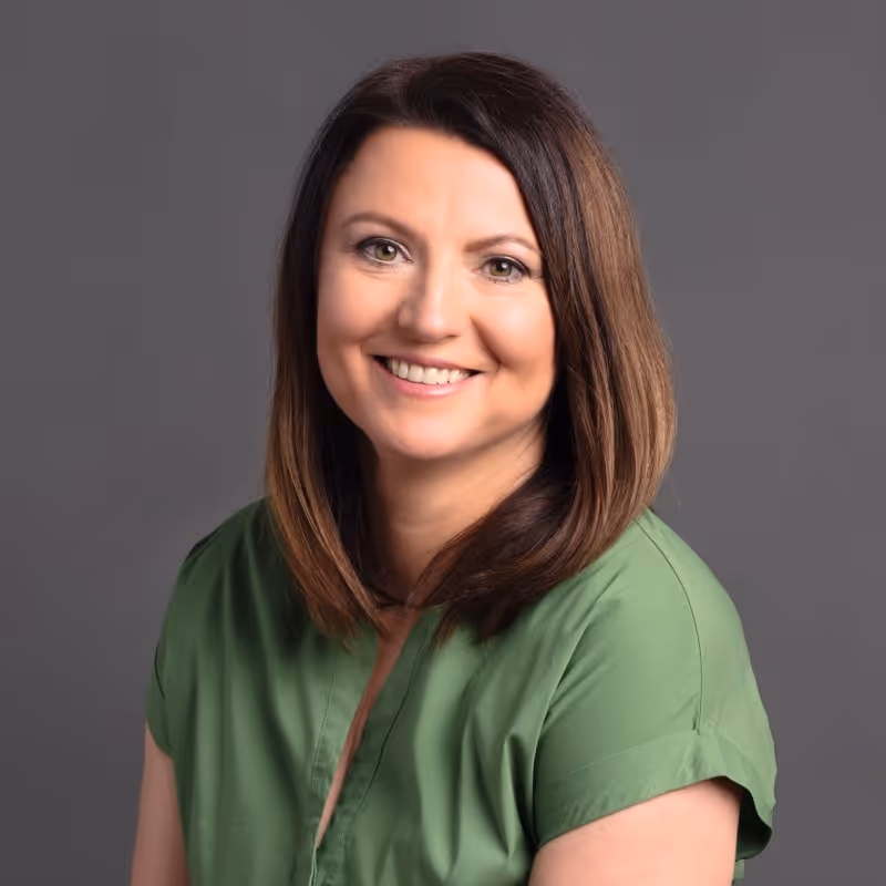 Mosolygó barna hajú nő zöld ingben szürke háttér előtt.