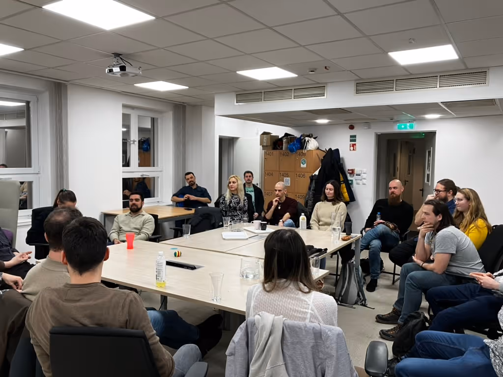 Emberek egy kör alakú asztal körül ülnek egy tárgyalóteremben.