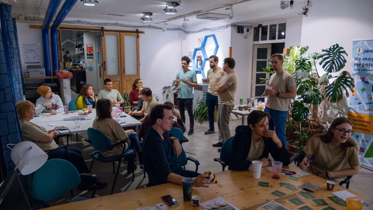 Csoport fiatal felnőttek együtt ül egy világos teremben, néhányan beszélgetnek, mások jegyzetelnek vagy figyelnek.